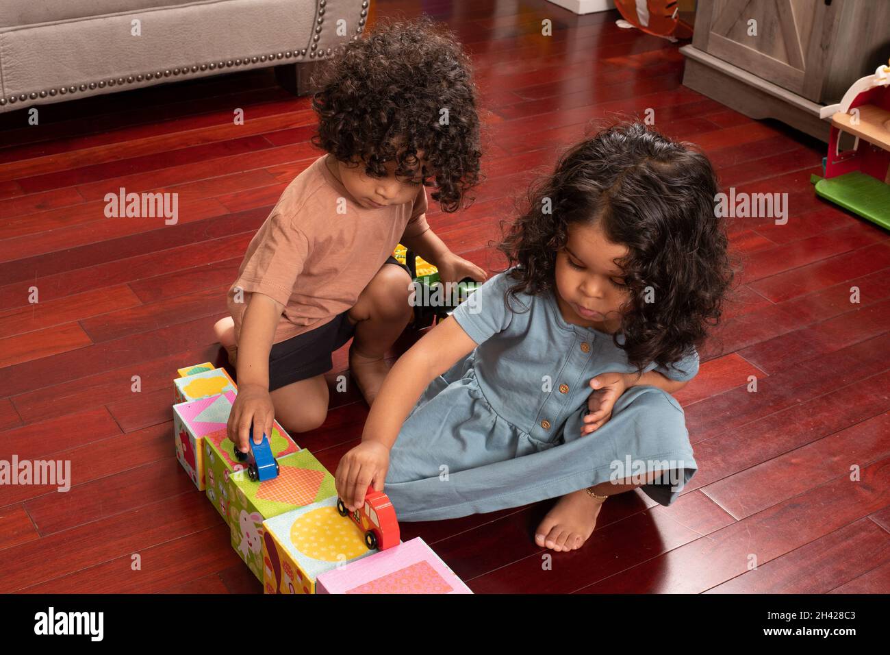 Two year old fraternal twins, boy and girl,  playing with toy cars driving them on road made of cardboard blocks Stock Photo