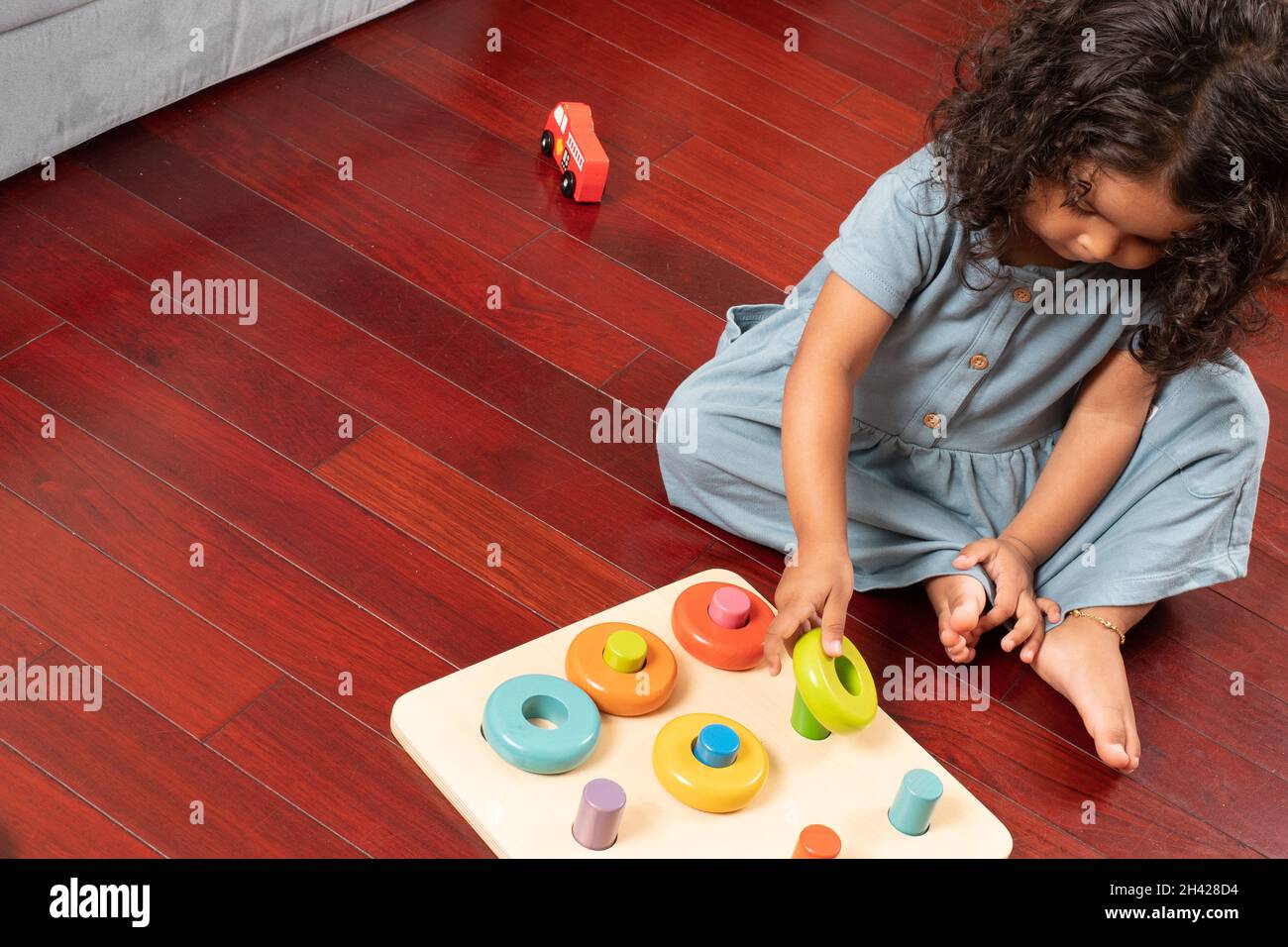 2 year old toddler girl playing with peg and circles geometric board turning wrist to place circle on peg Stock Photo