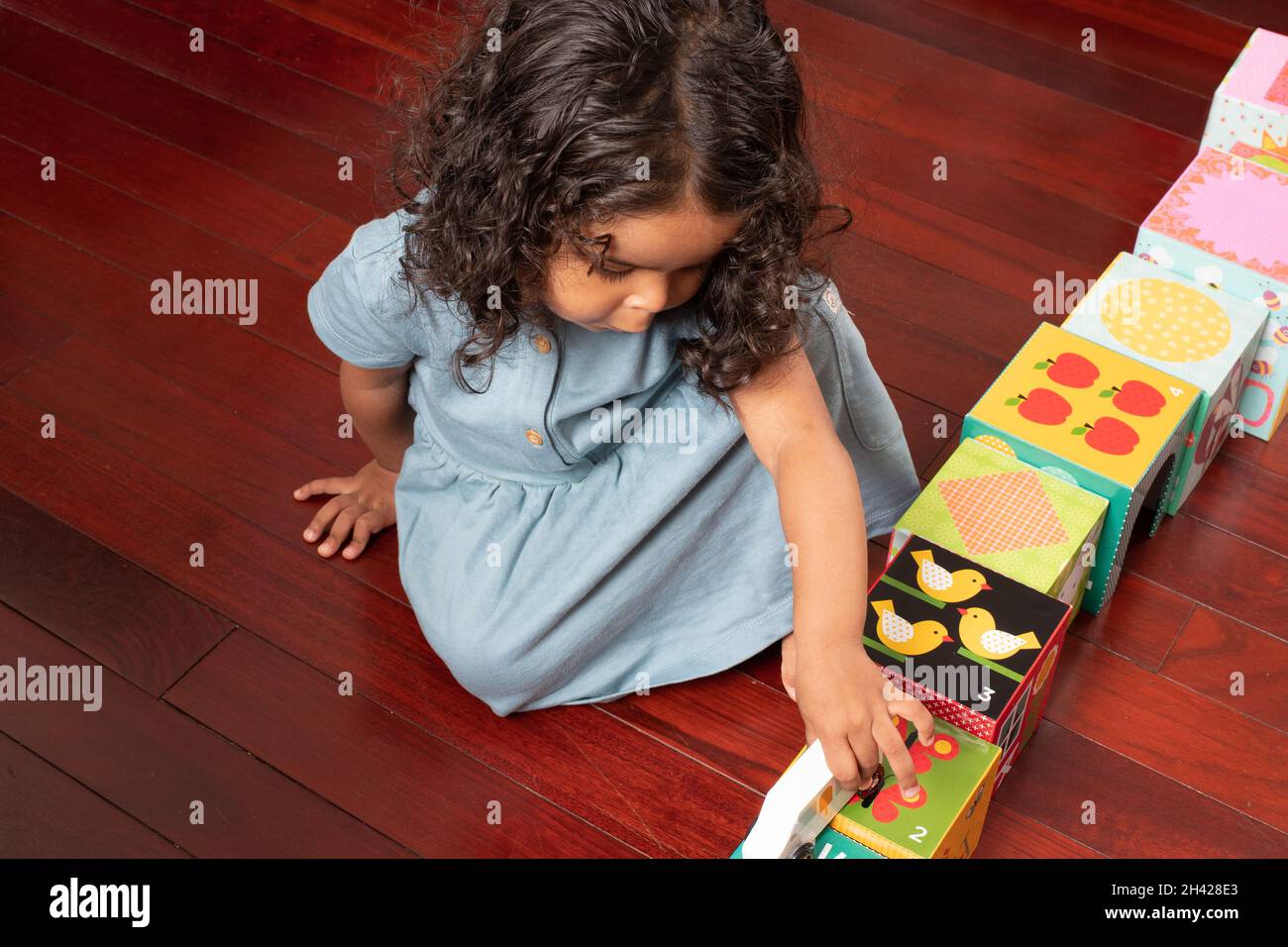 2 year old toddler girl playing with toy car and road made out of cardboard blocks Stock Photo