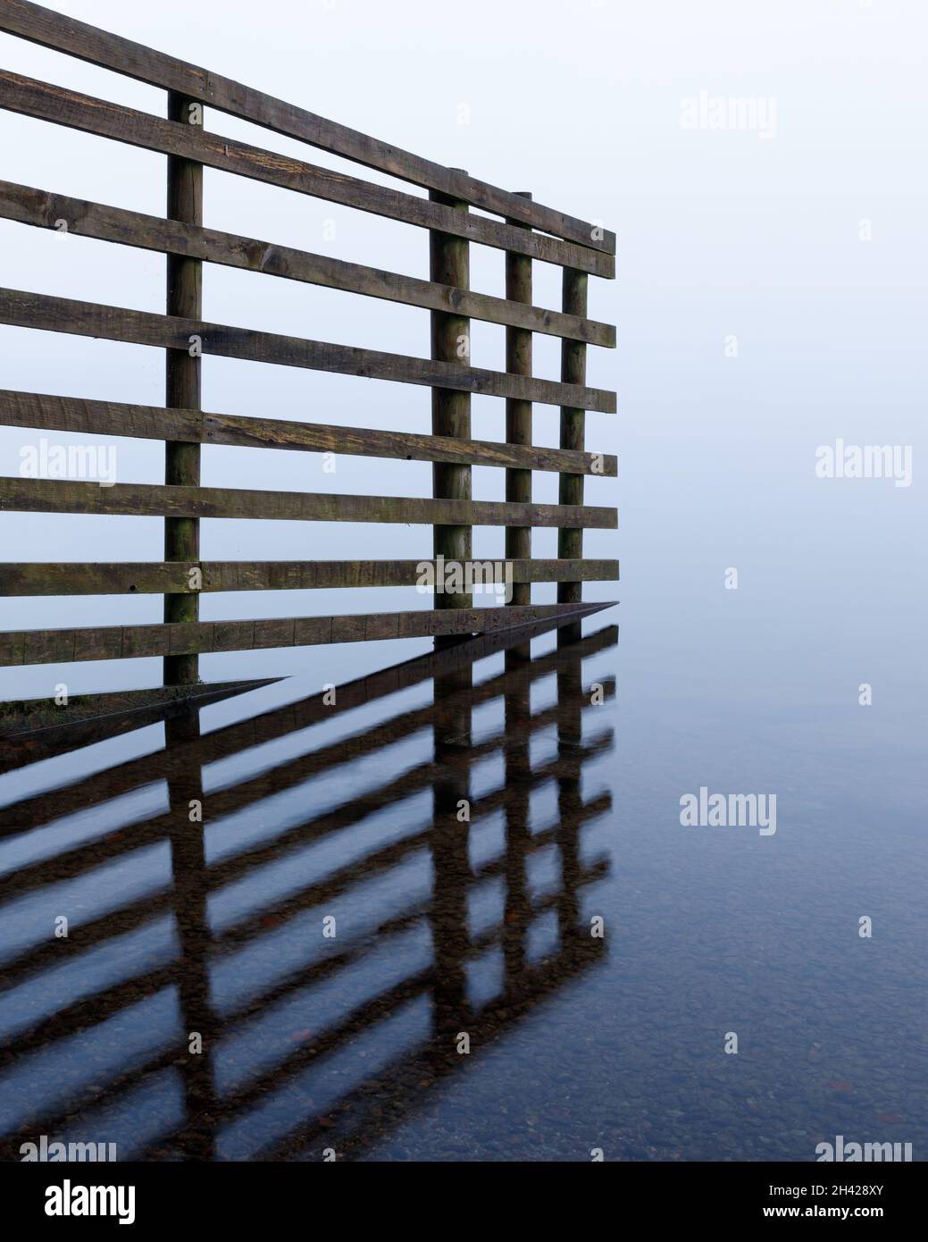 Grasmere, Cumbria, UK, October 1st 2020: On a misty morning a fence made from slats of wood enters the water of Grasmere in the Lake District. Stock Photo