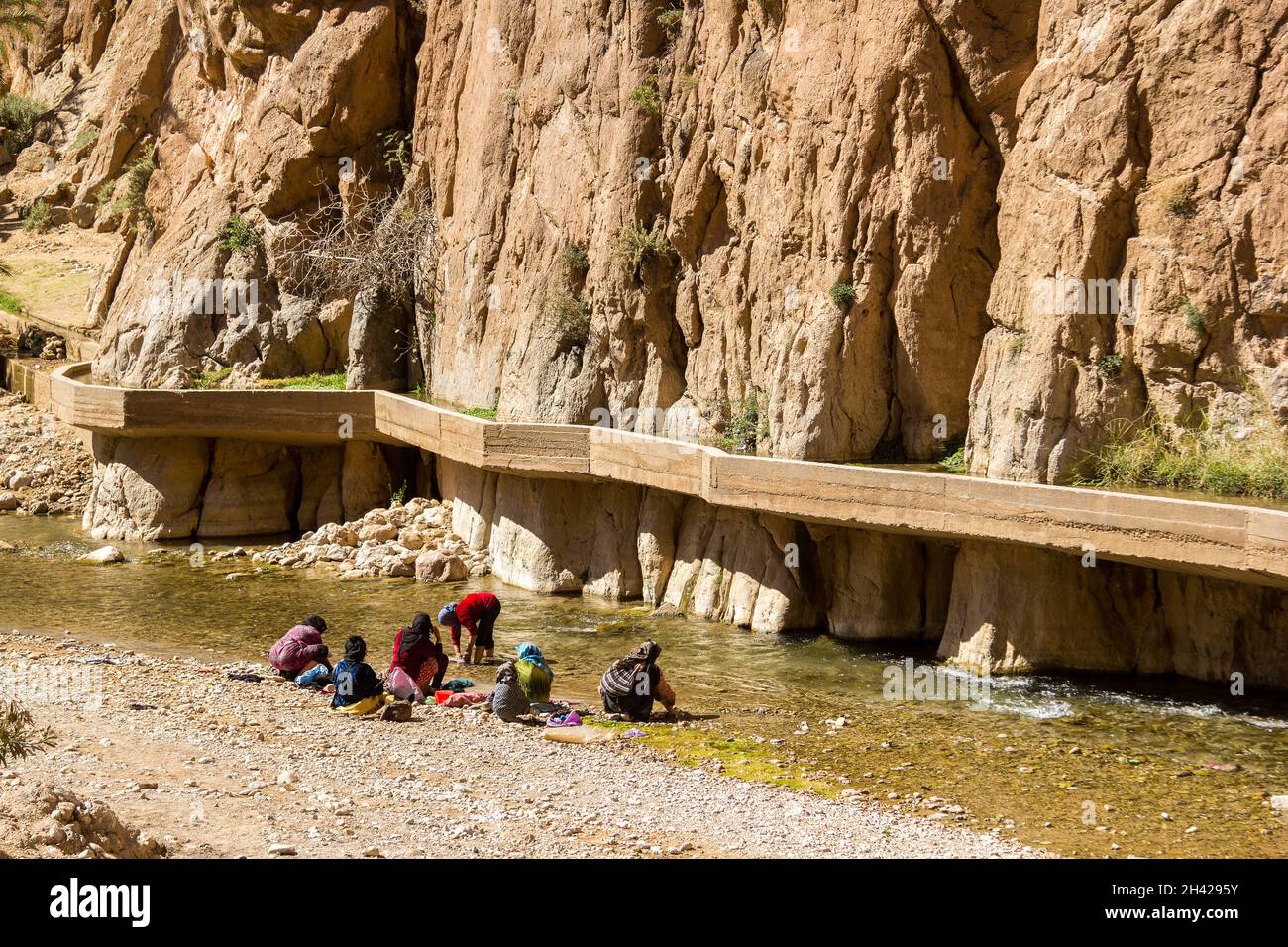 Todra, Morocco - February 25, 2019: Women with children (unidentifiable) in colorful costumes are doing laundry at the river side in the famous Todra Stock Photo