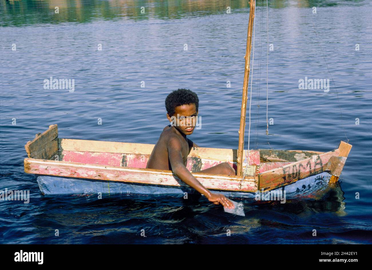Africa, Egypt, Aswan, River Nile 1976. A boy in a homemade boat with an eye painted on the prow. The 'all-seeing eye'.  The Eye of Horus was a symbol of protection, health, and wholeness. Stock Photo