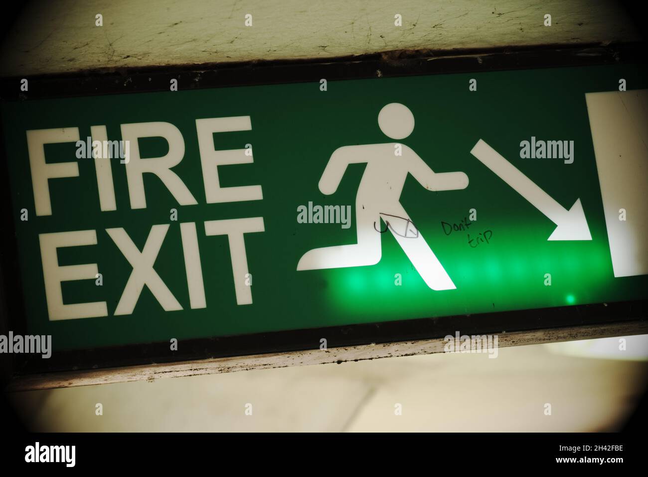 Fire Exit illuminated sign with rude graffiti Stock Photo