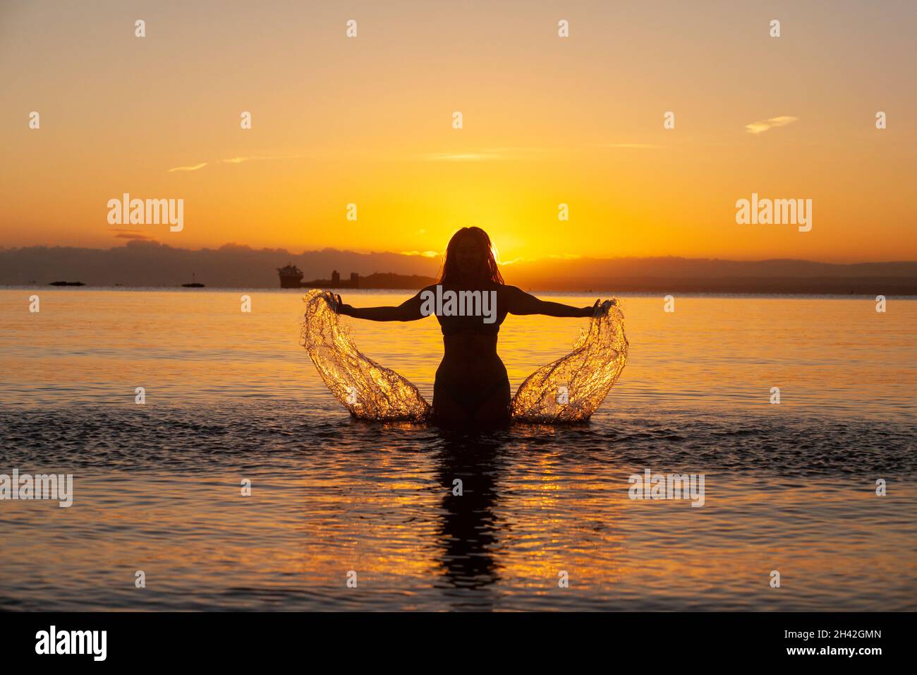 A woman splashing the water on a cold October sunrise in Scotland Stock Photo