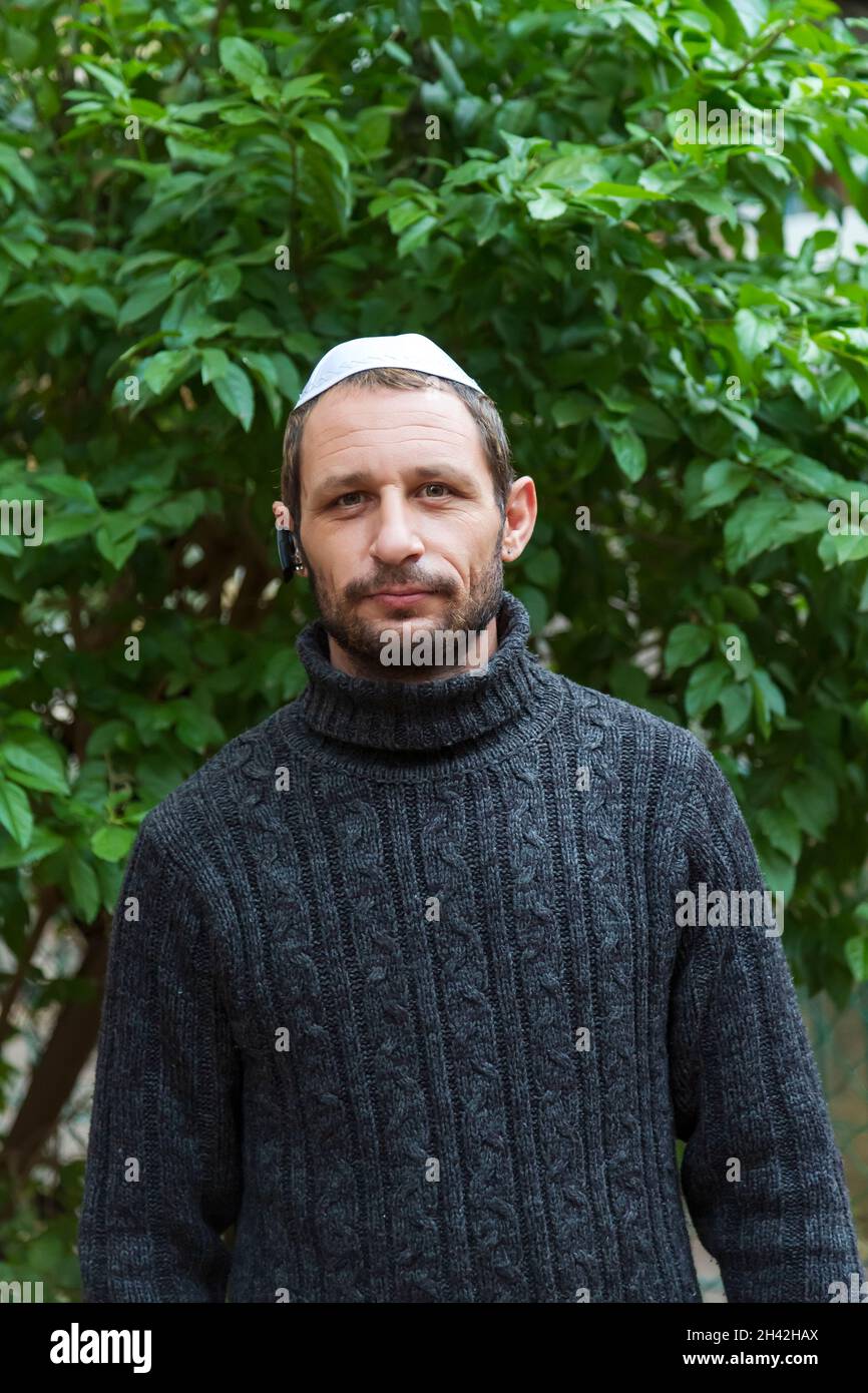 Jewish man wearing kippah in Hebrew or yarmulke (cloth cap traditionally worn by Jewish males) with green trees in the background, beard wearing black Stock Photo