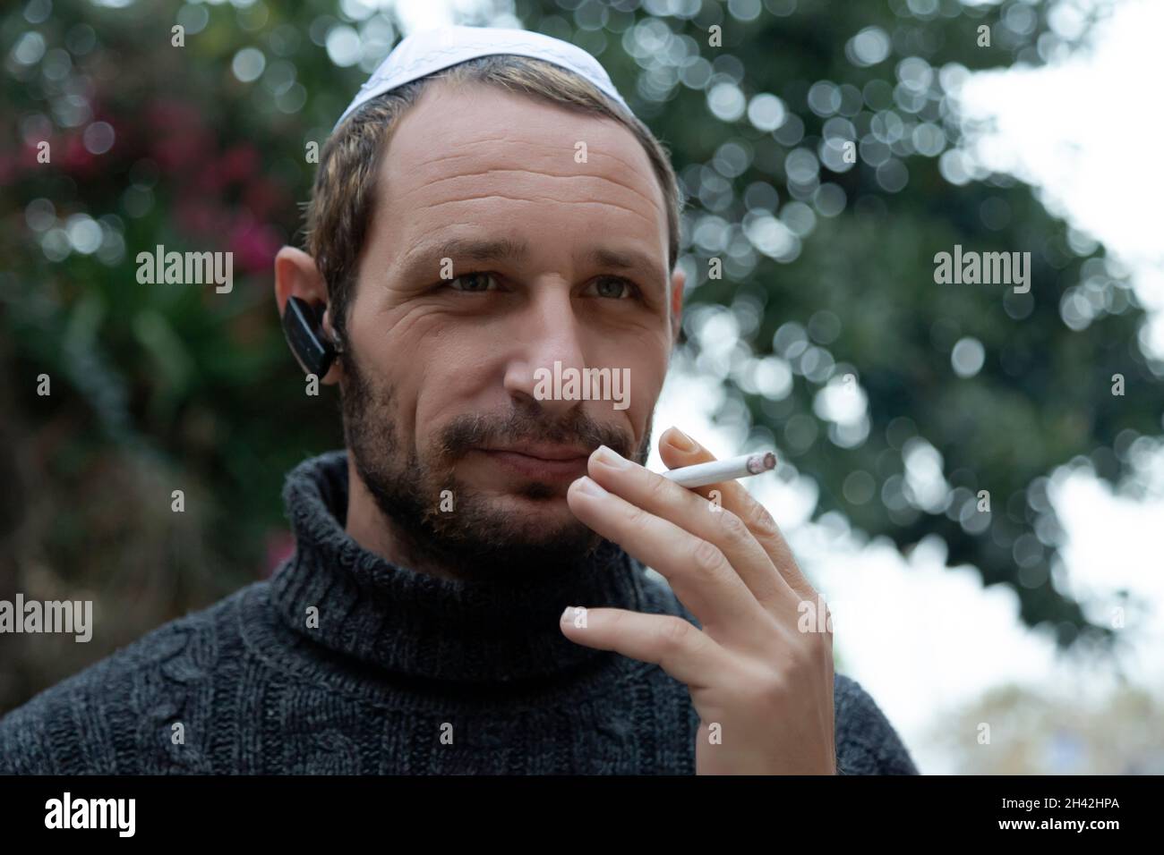 Jewish man wearing kippah in Hebrew or yarmulke with green trees in the background, beard wearing black sweatshirt. Portrait of a middle aged man with Stock Photo