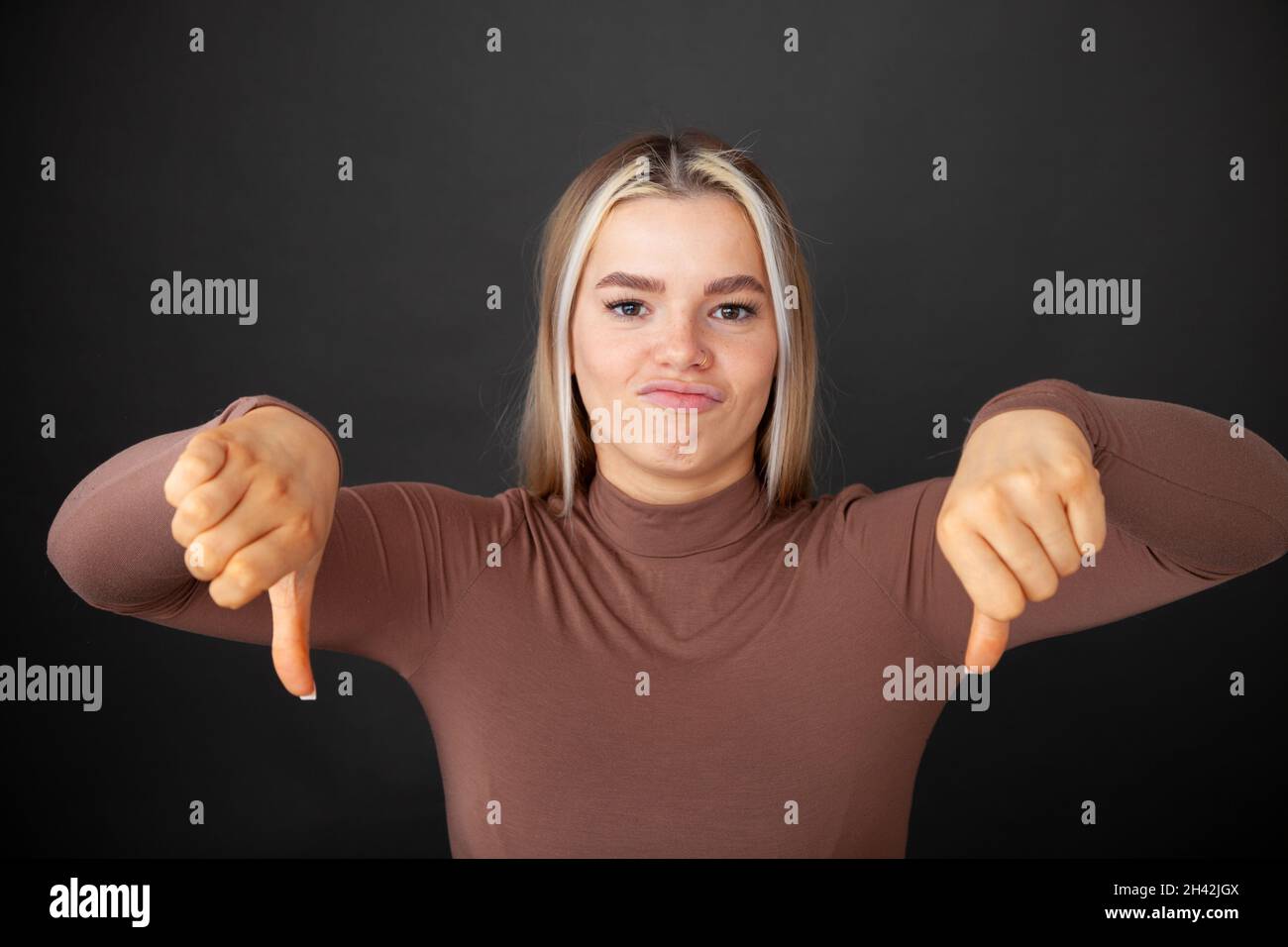 Portrait of disappointed young woman standing with thumbs down Stock Photo