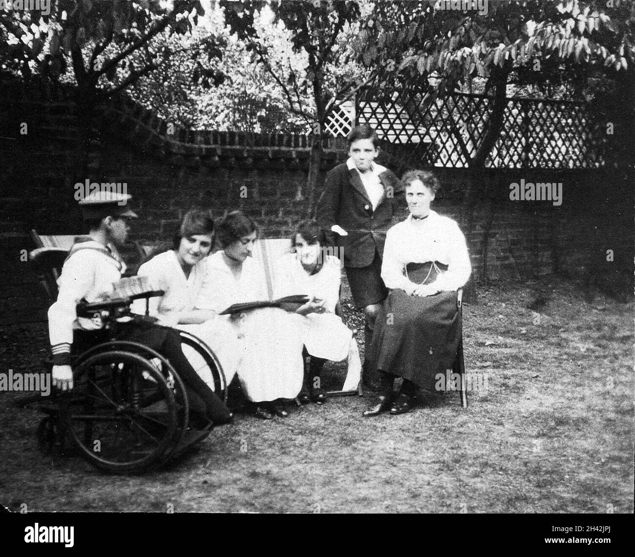 A physically handicapped boy sitting in a wheelchair in a garden. Photograph, ca. 1910/1925. Stock Photo