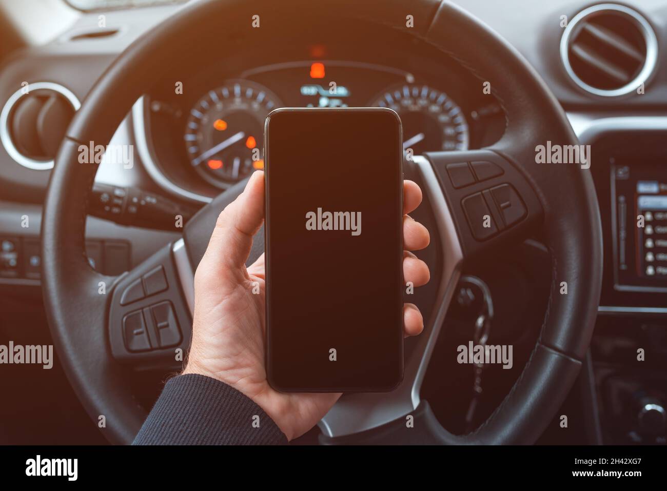 Car driver holding mobile smart phone over steering wheel, blank black screen as copy space, selective focus Stock Photo