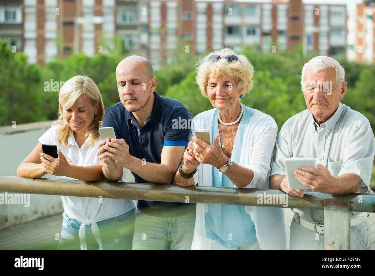 Smiling mature couples using gadgets in park Stock Photo