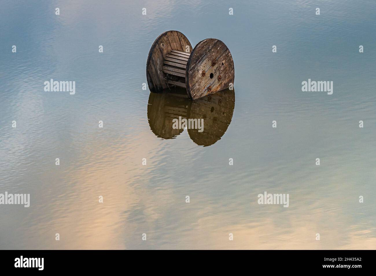 a wooden circle in a large puddle of water with a reflection of the sky on the small small waves of water in the large expanse of water Stock Photo