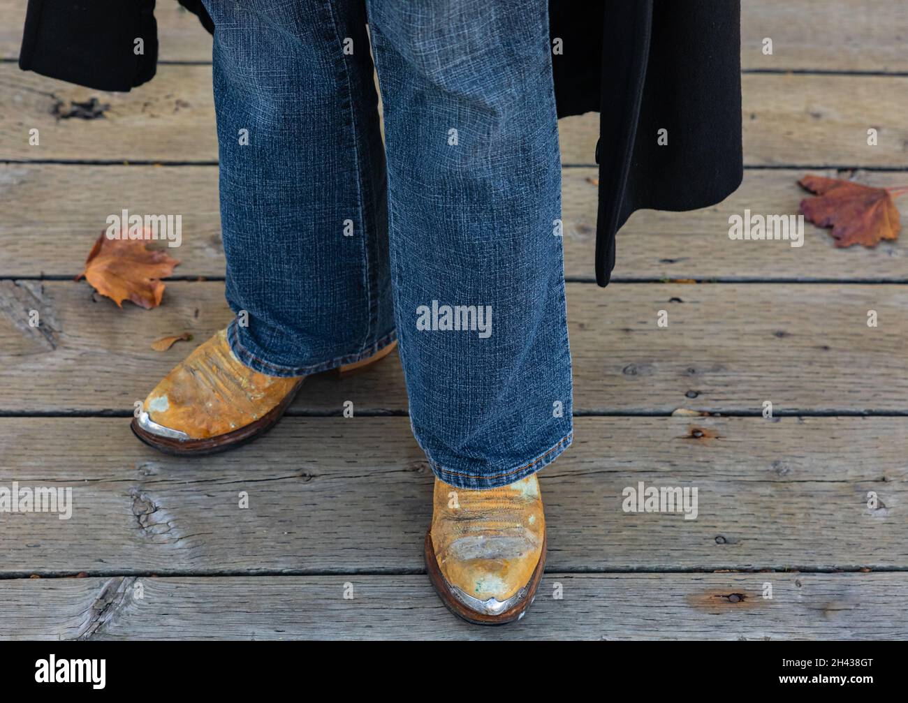 Cowboy boots and jeans, close up of details of Western style clothing on man outdoor. Autumn season. Street view, selective focus. Stock Photo