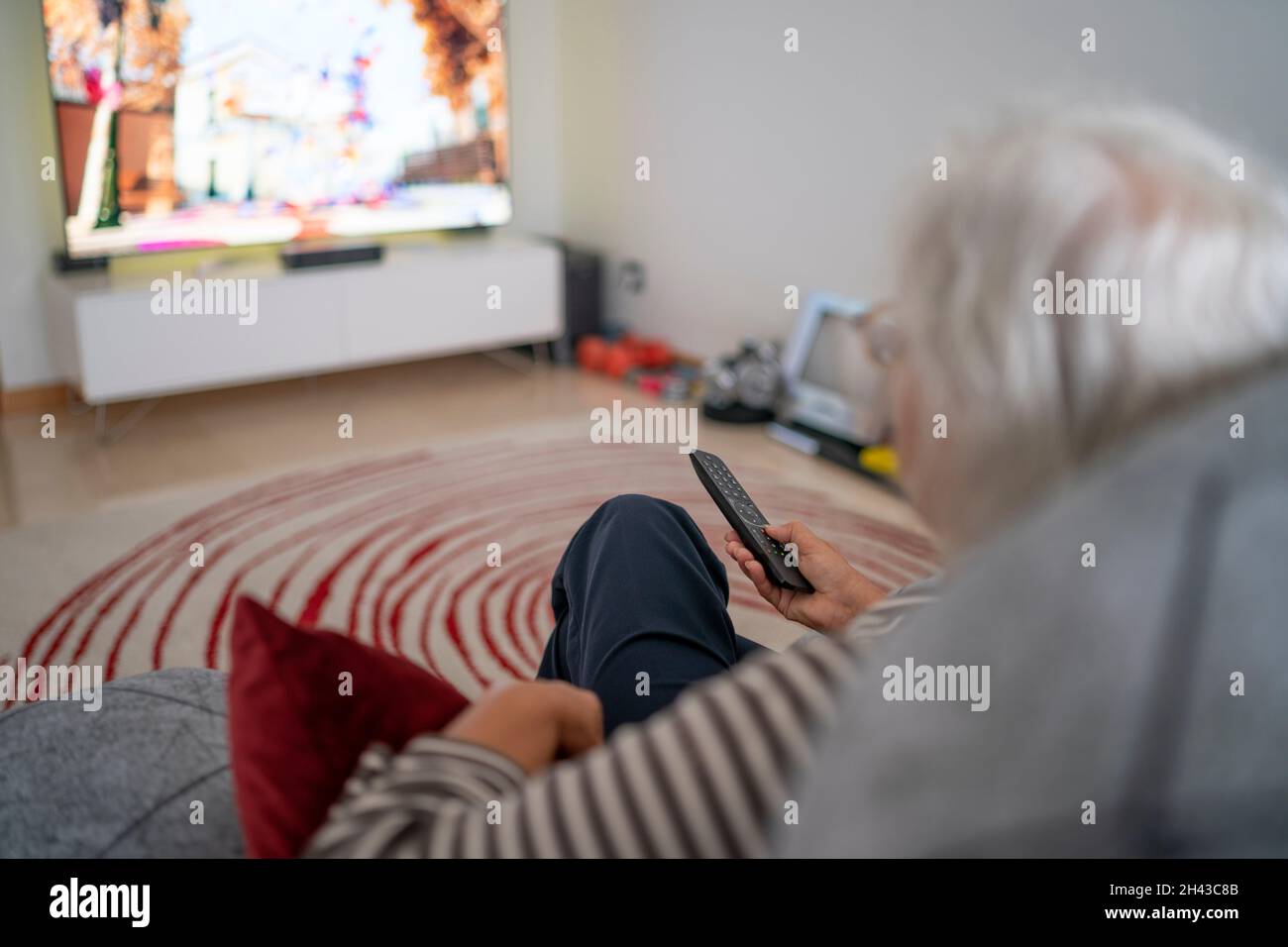 Selective focus photo of a mature woman holding the TV remote while watching television at home Stock Photo