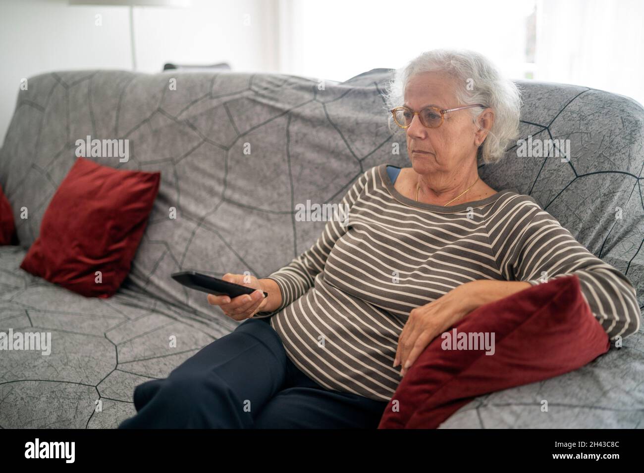 Mature woman holding the TV remote while watching television at home Stock Photo