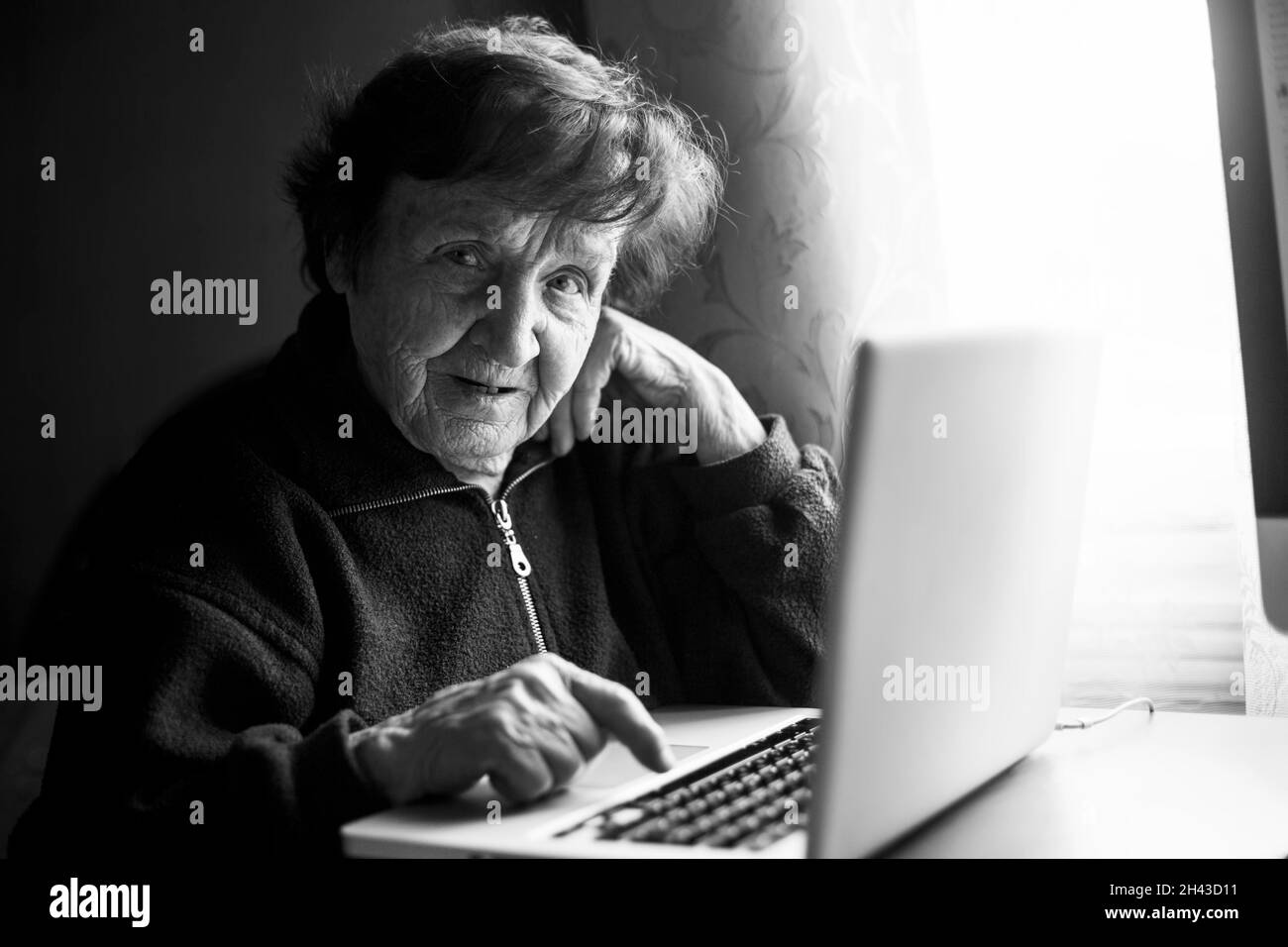 An old woman studying working on the computer in her home. Black and white photo. Stock Photo