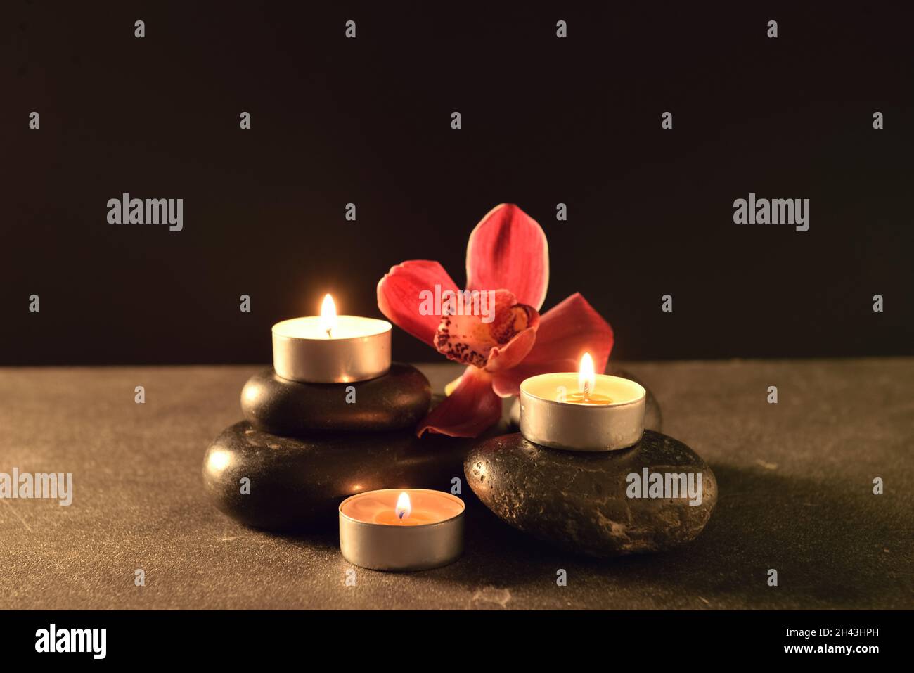 Burning candles with flower and spa stones on table against black ...