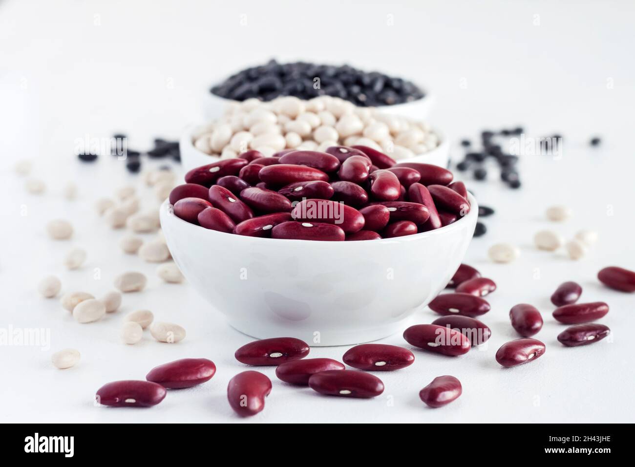 Assortment of beans in a white bowl on white background. Red kidney beans, white beans and black beans Stock Photo