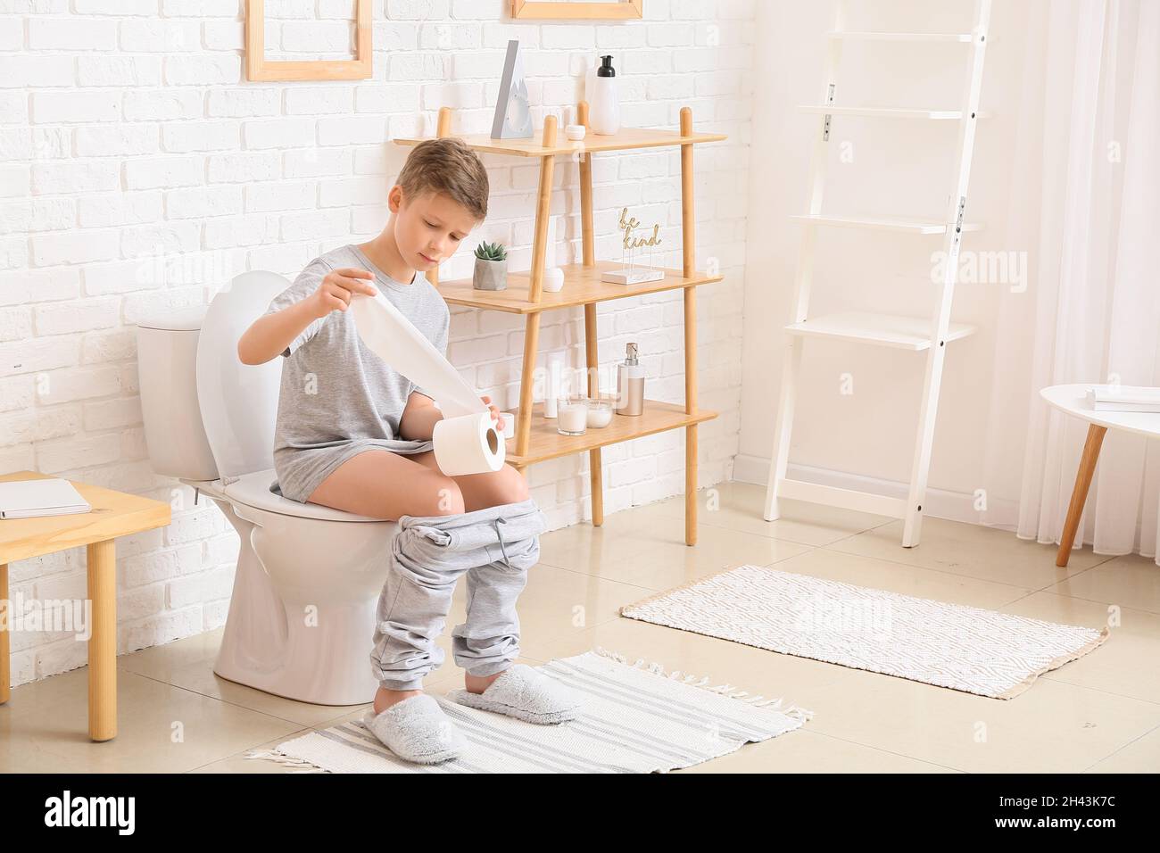 Little boy with paper sitting on toilet bowl in bathroom Stock Photo