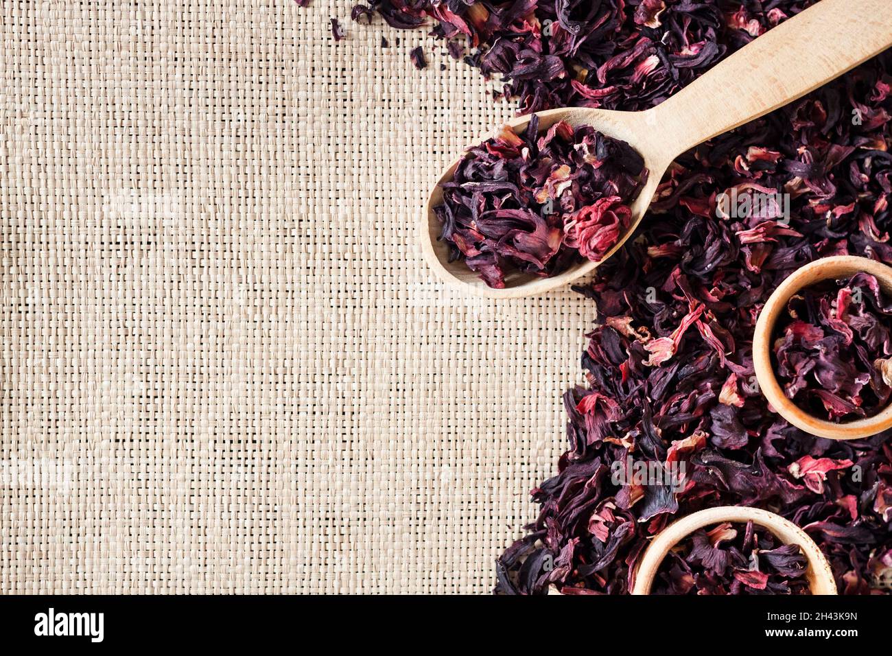 Straw mat background with hibiscus tea. Wooden spoon and small cups with dry  hibiscus petals. Flat lay, top view, copy space Stock Photo