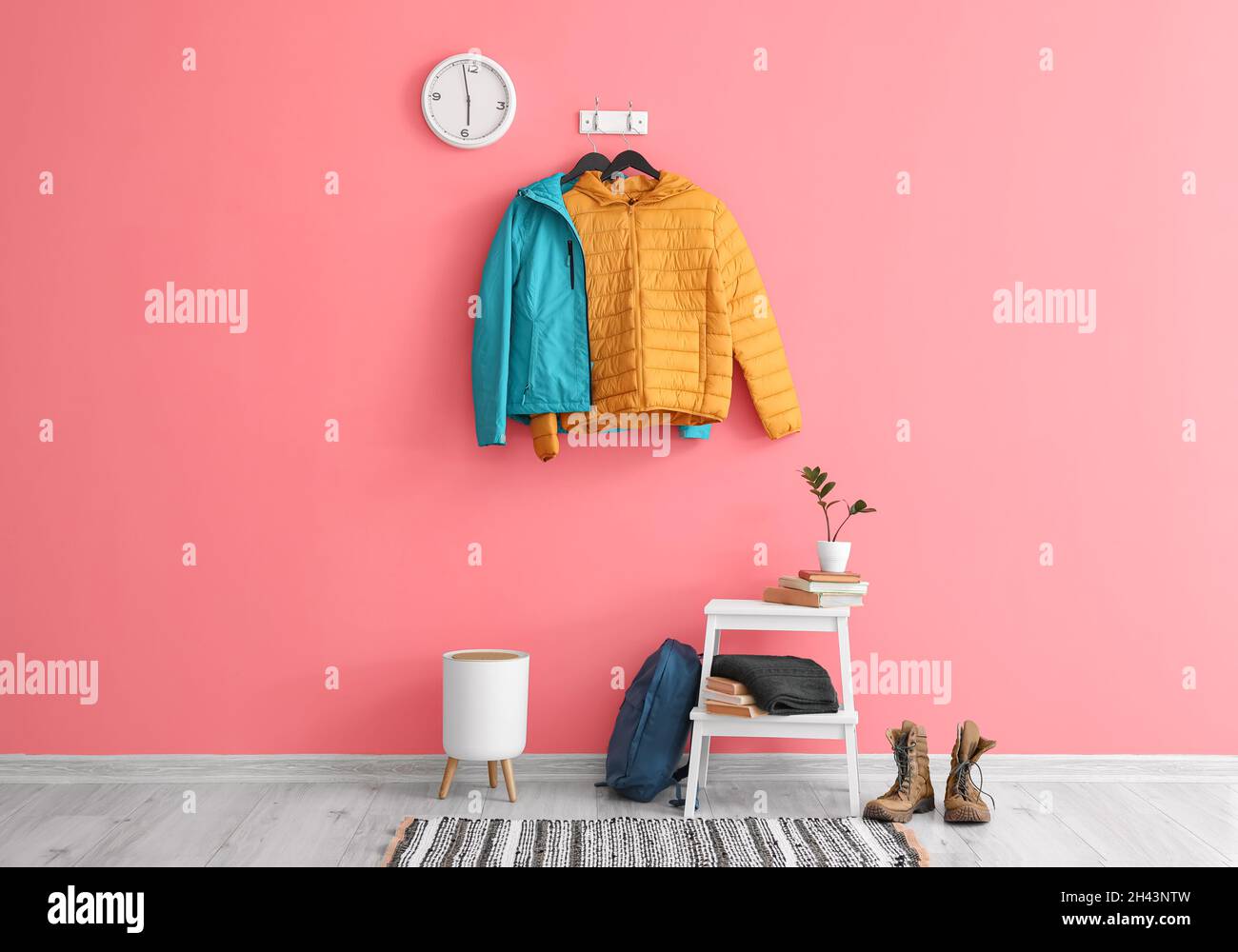 Blue and yellow jackets hanging on pink wall in stylish hallway Stock Photo