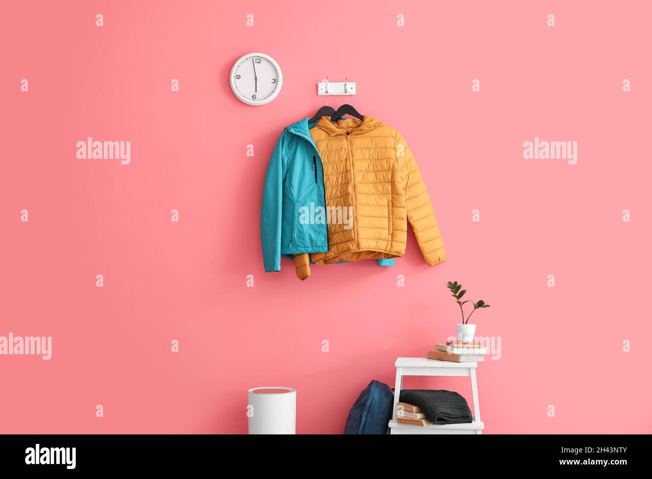 Blue and yellow jackets hanging on pink wall in stylish hallway Stock Photo