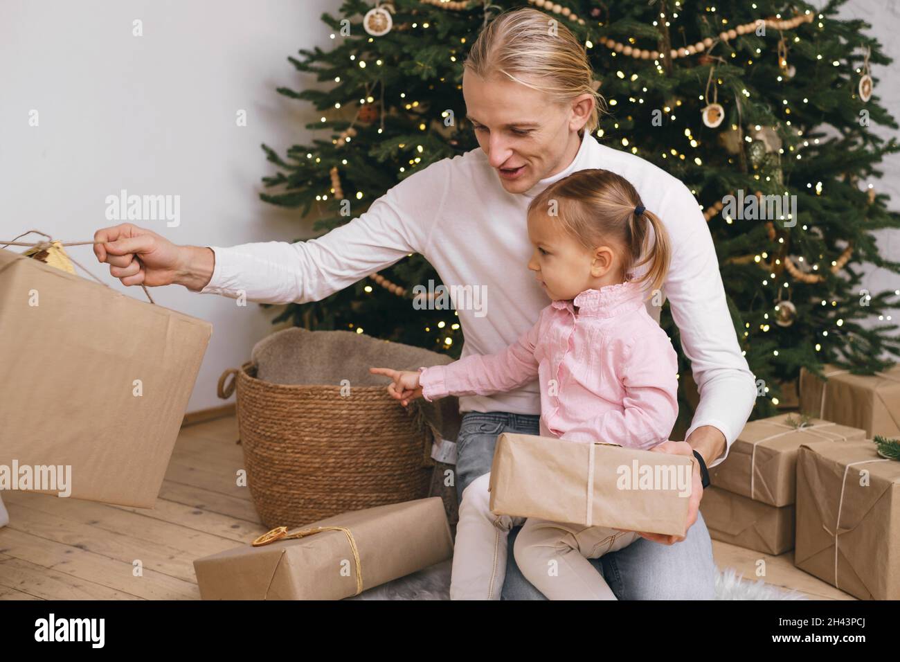 Father with child getting ready for Christmas, wrapping gift boxes near tree. Happy family dreaming of celebrations and presents at stylish Stock Photo