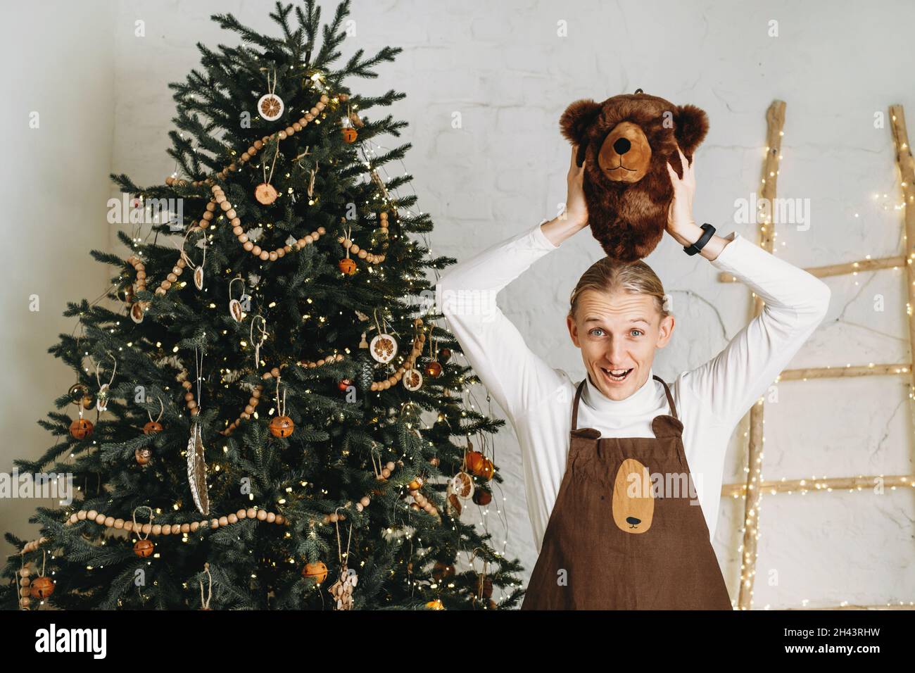 Funny man in front of Christmas tree ready for celebration with gifts in bear mask and costume. Surprise, carnival party for adult  Stock Photo