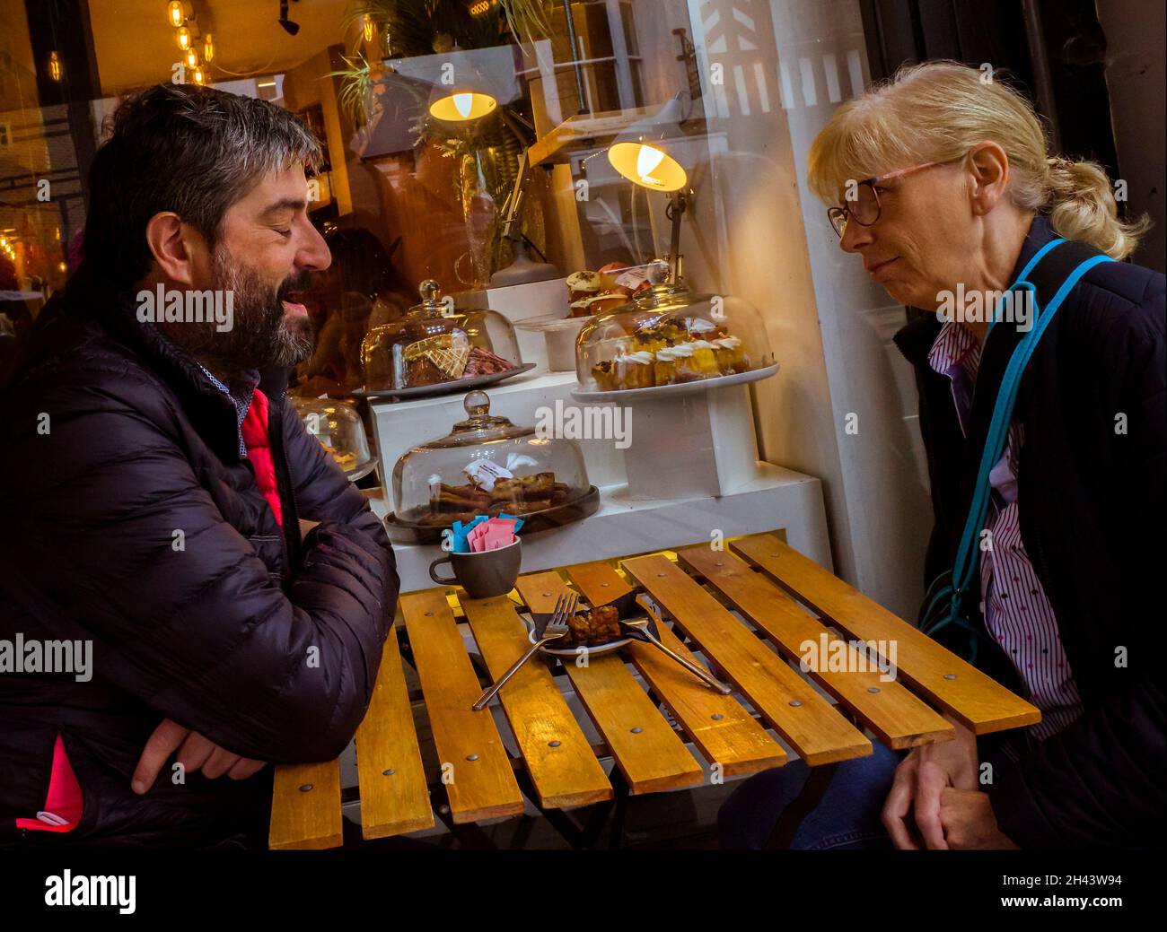 A man and woman deep in conversation share their thoughts and a cake outside a coffee shop. Stock Photo