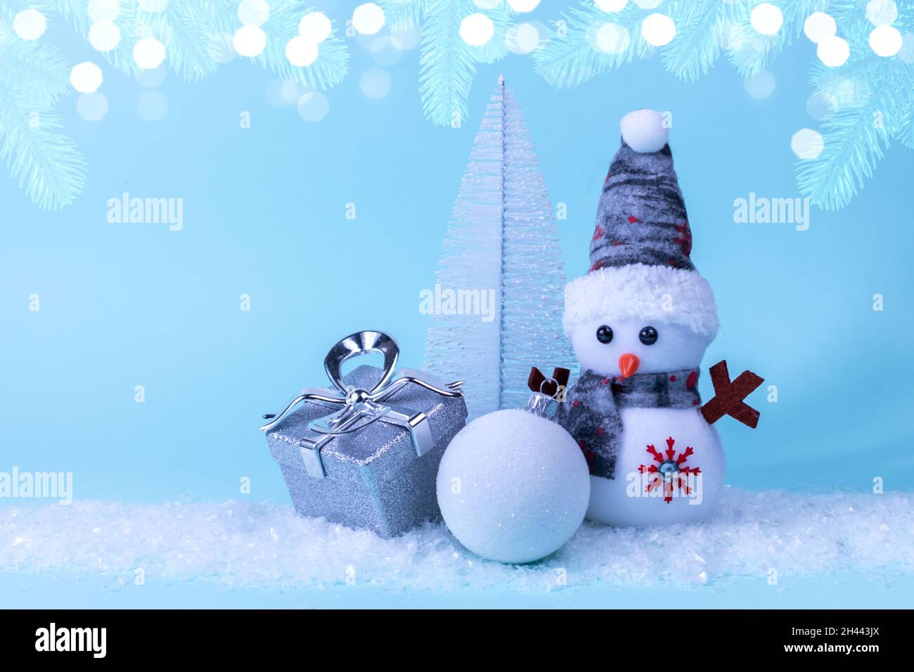 Snowman, gift, Christmas tree, Christmas ball on white snow on a blue background with Christmas tree branches and garlands. Christmas New Year card Stock Photo