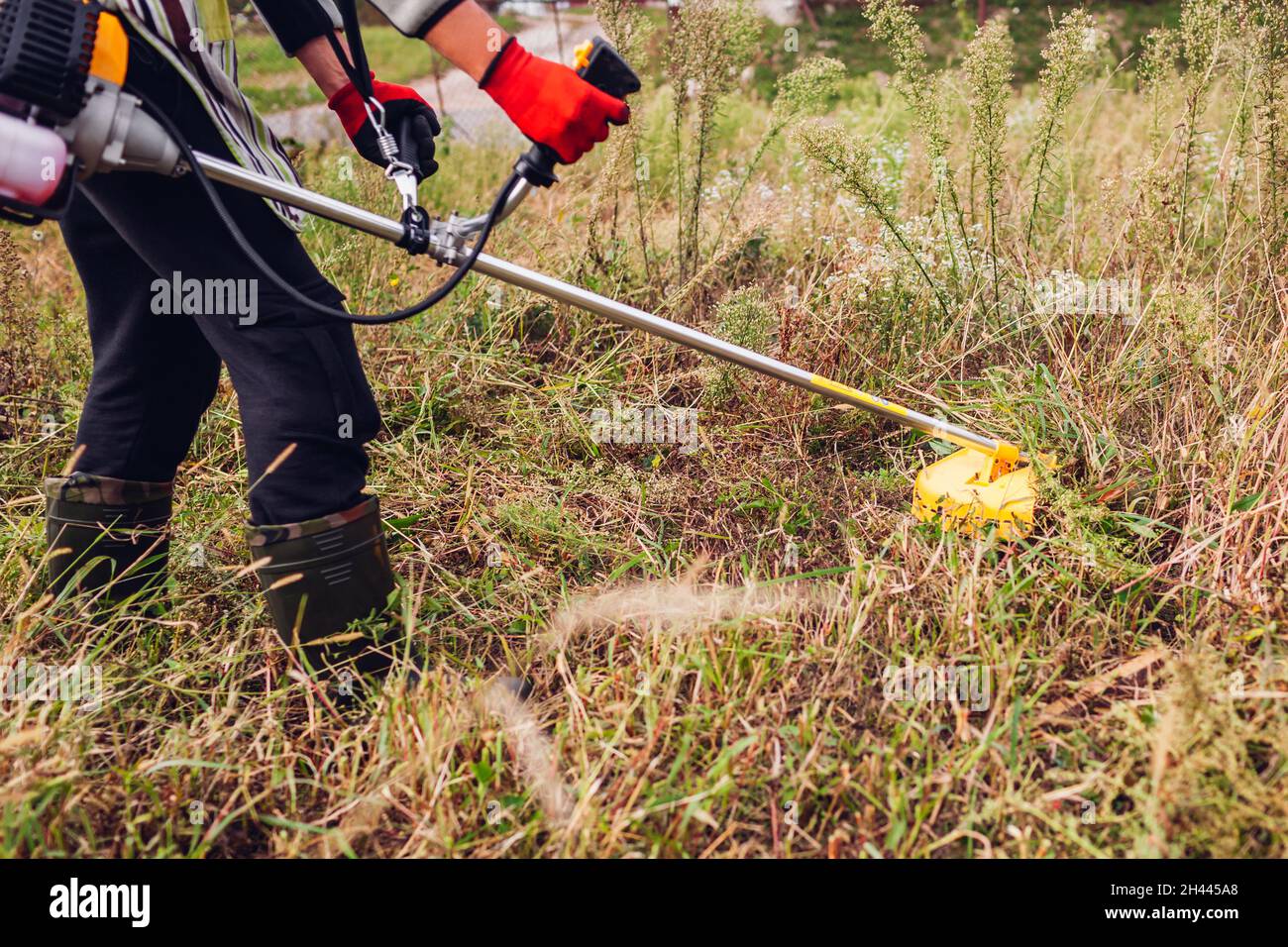 Gardener mowing weeds with brush cutter. Worker trimming dry grass with manual gasoline trimmer with metal blade disk Stock Photo