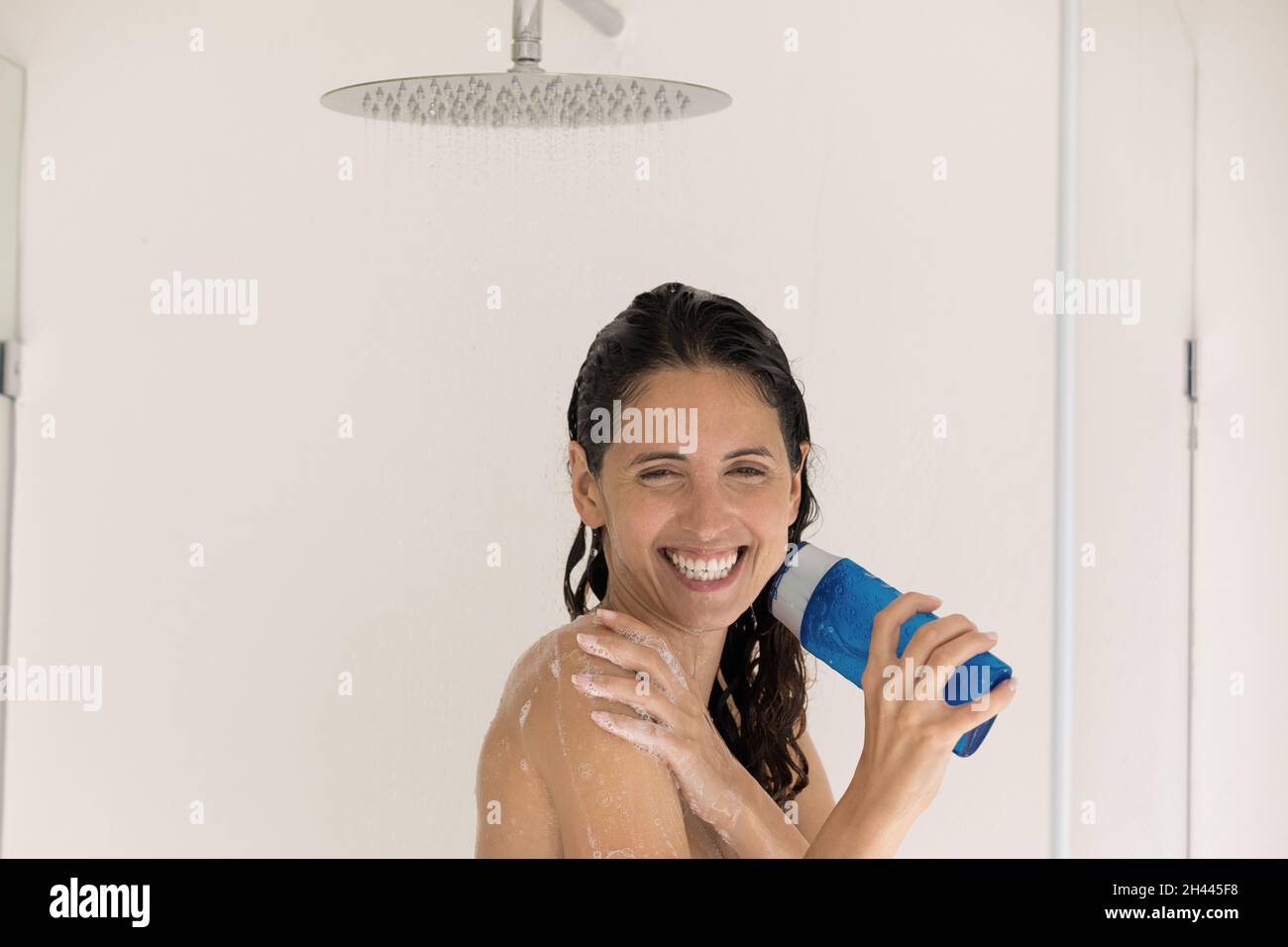 Woman holds shampoo bottle sing song while take a shower Stock Photo