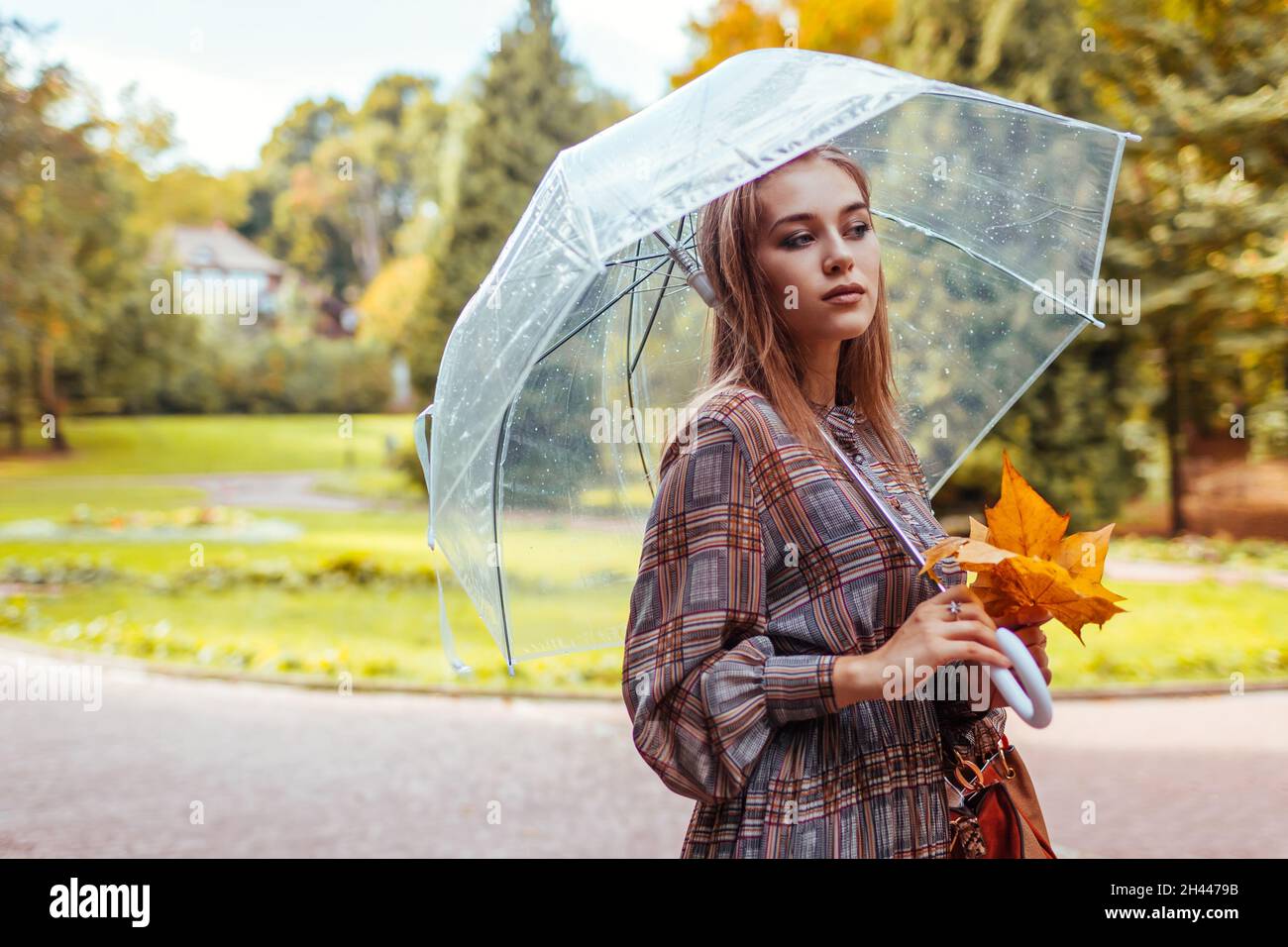 Portrait of young woman walking in park with transparent umbrella ...