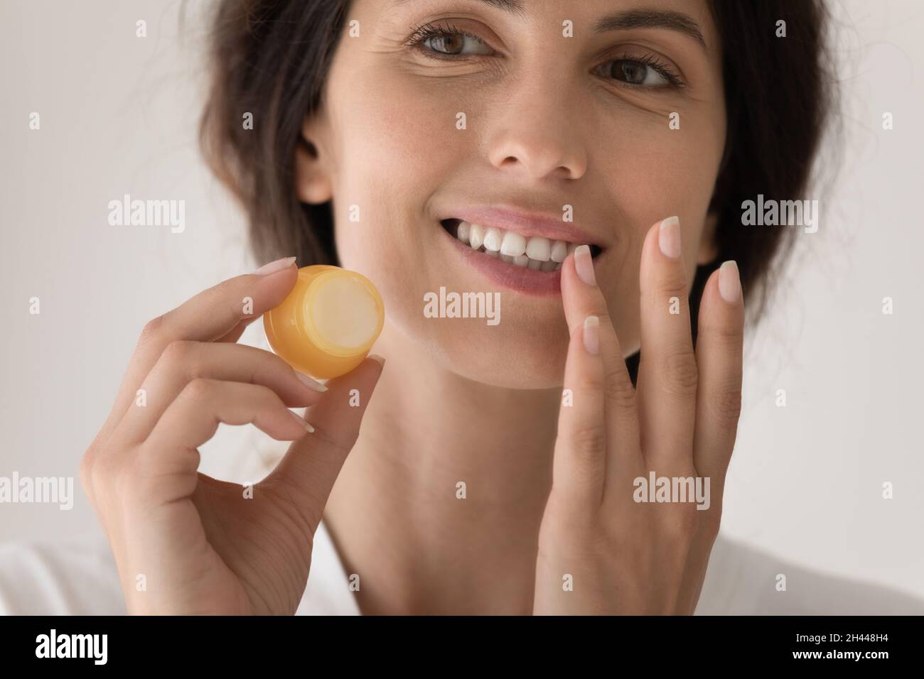 Closeup young beautiful woman holding jar apply balm on lips Stock Photo