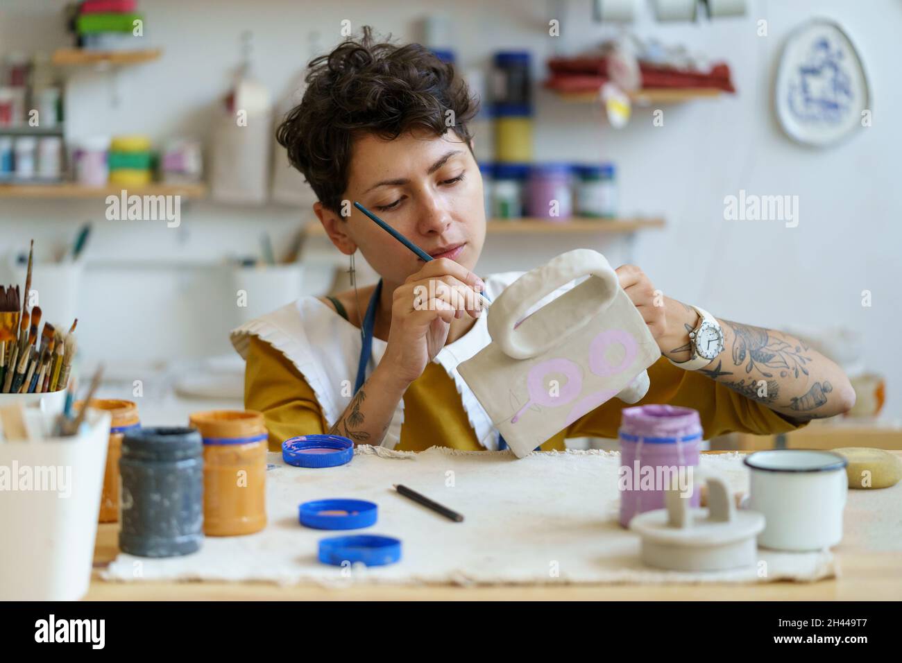 Creative artisan woman painting pottery jug, artistic process in