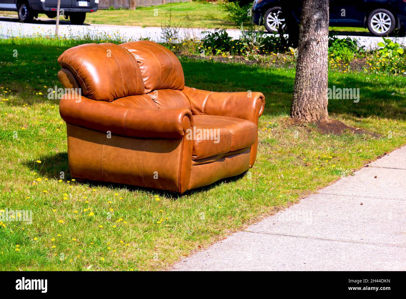 Discarded leather loveseat by a sidewalk waiting for someone to pick it up. Stock Photo
