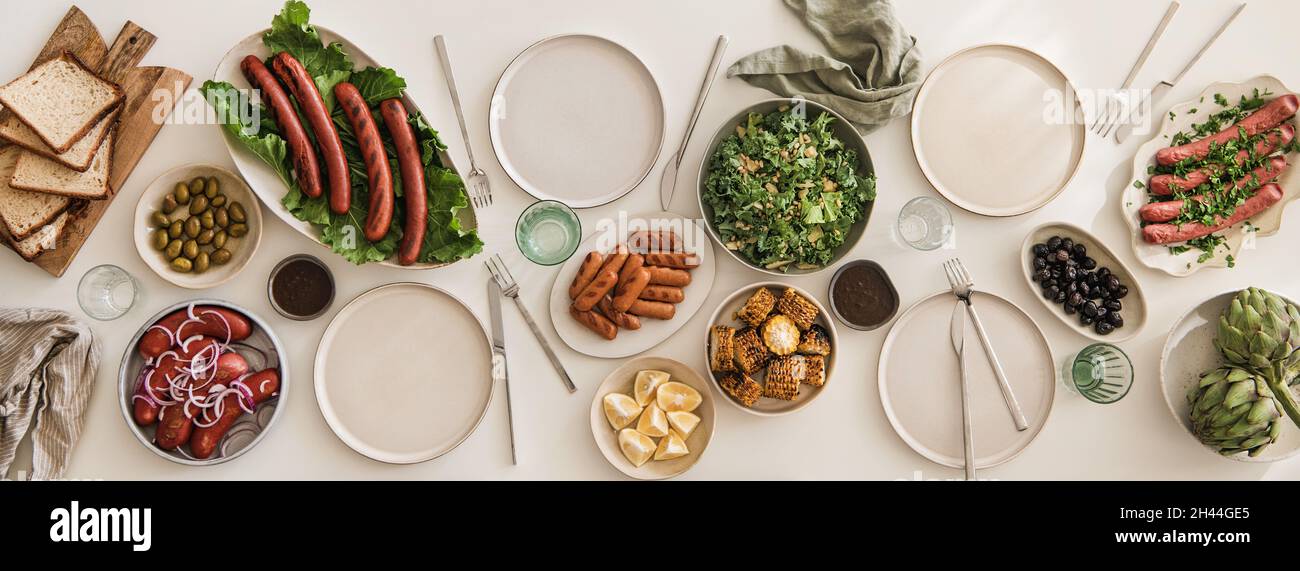 Flat-lay of white table with grilled pork sausages and snacks Stock Photo