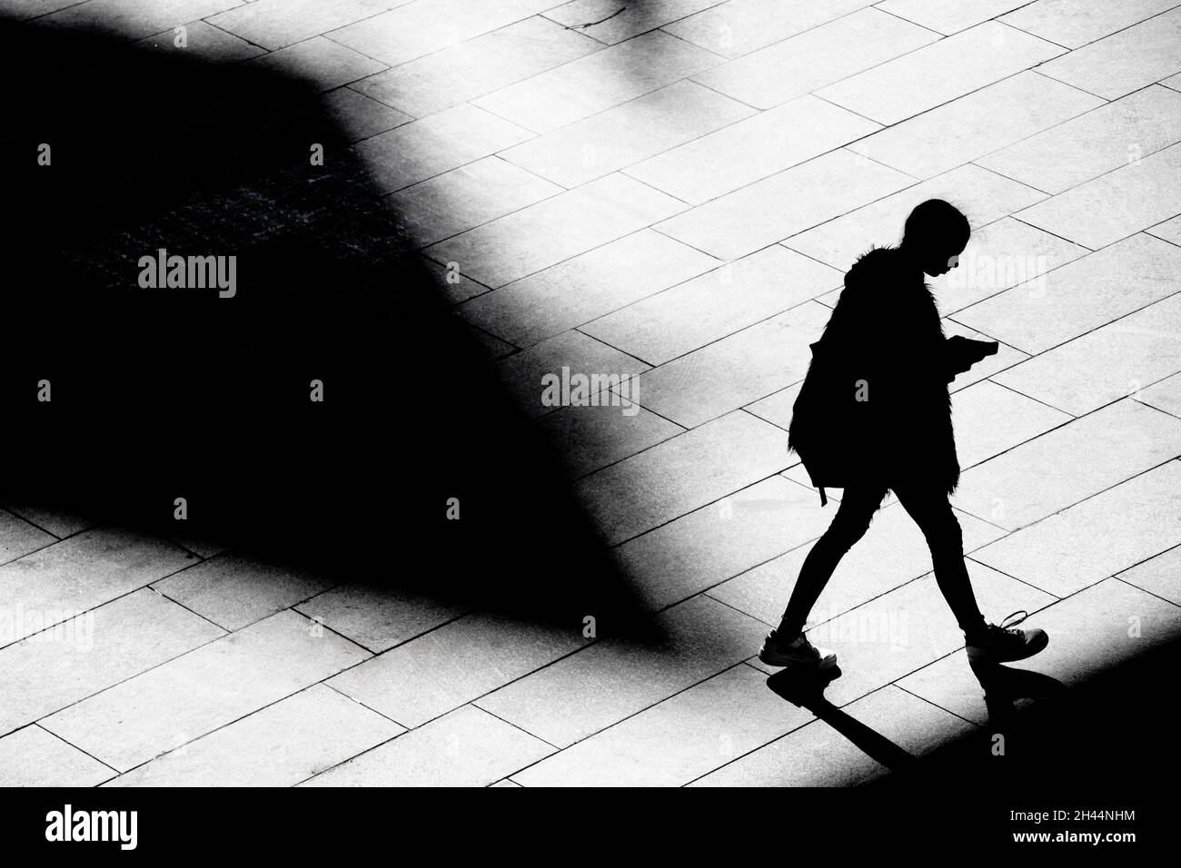 Shadow silhouette of teenage girl watching cell phone while walking city street sidewalk, in black and white from above Stock Photo