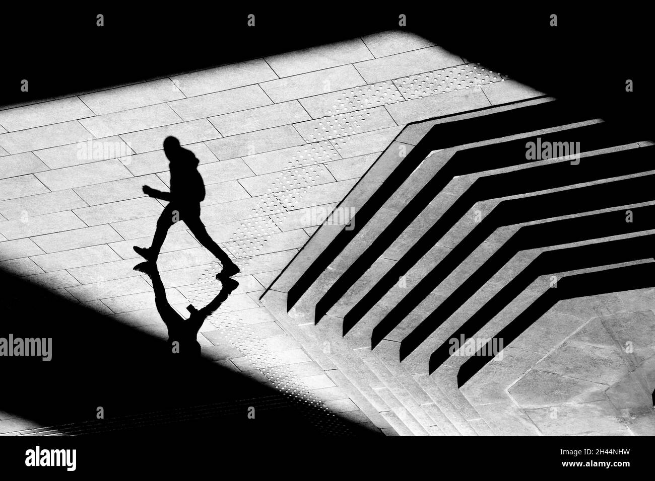 Shadow silhouette of teenage boy walking city street sidewalk, in black and white from above Stock Photo
