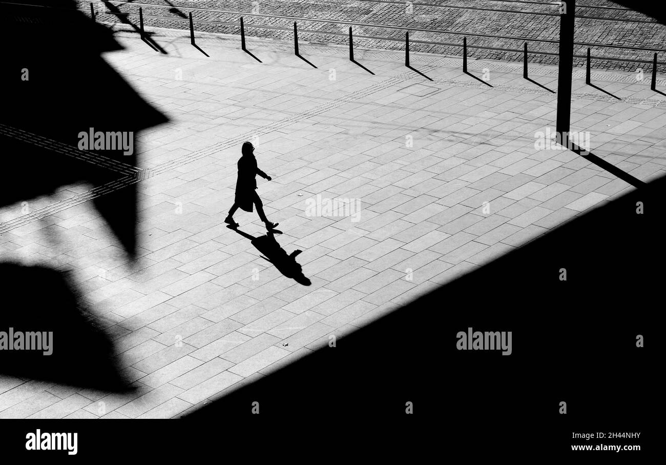 Shadow silhouette of a woman walking city street sidewalk square, in black and white from above with architectural shades Stock Photo