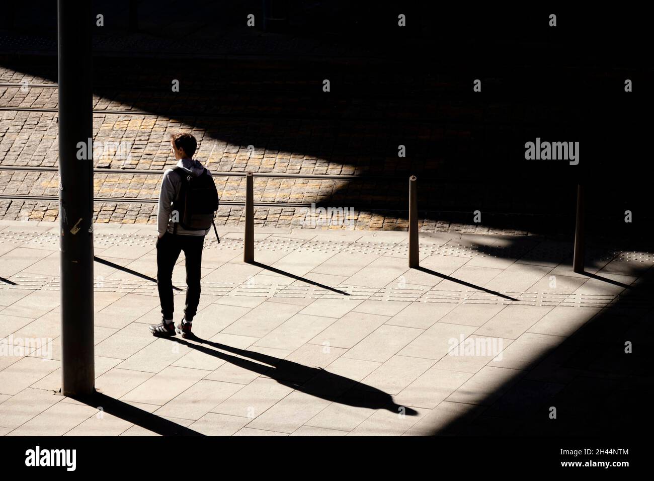 Belgrade, Serbia - October 26, 2020: One teenage boy standing alone waiting for a tram on bus stop in sunlight, high angle view from behind, with shad Stock Photo