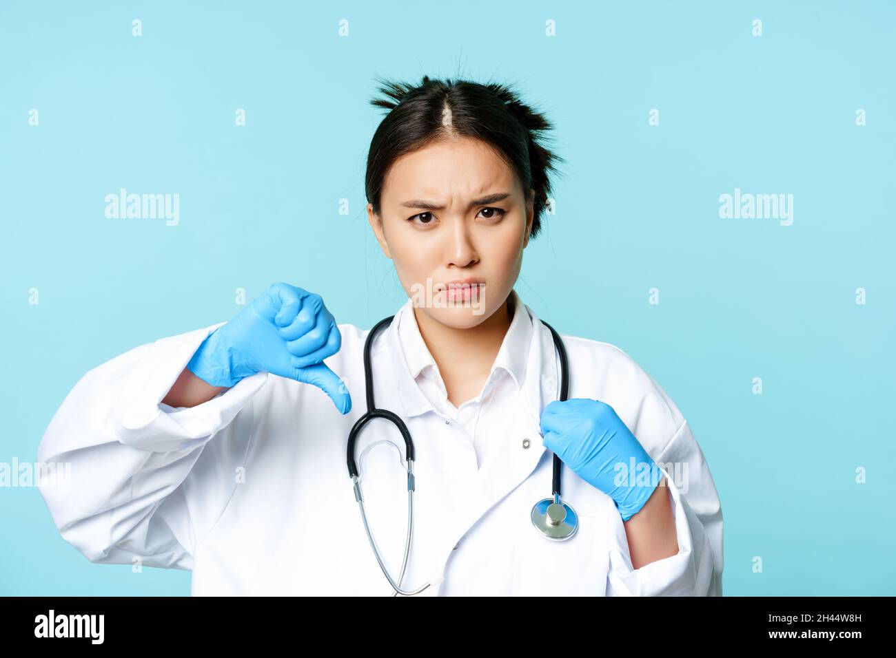 Angry asian woman doctor, physician in uniform and gloves shows thumbs ...