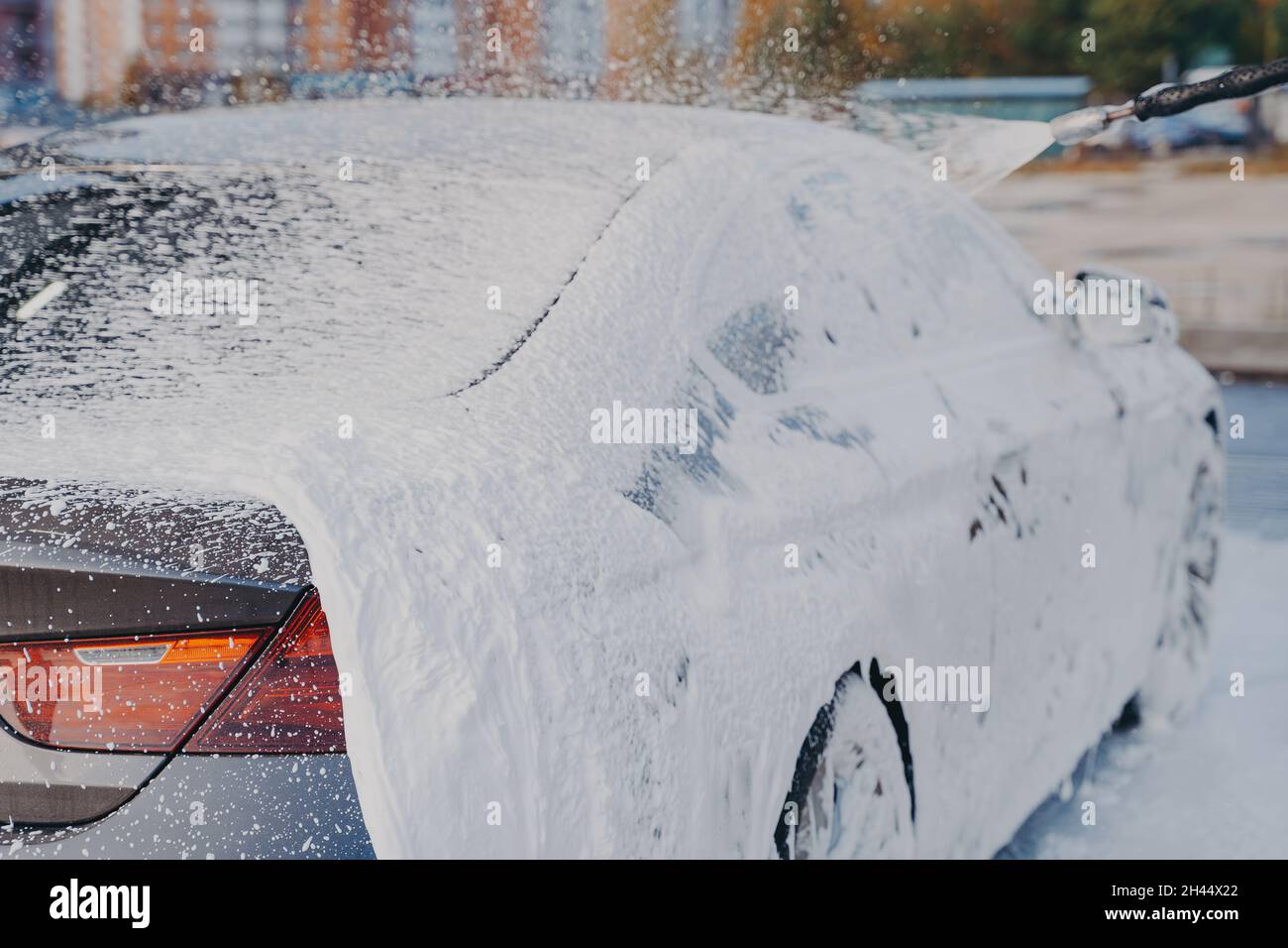 Car in white soap foam during cleaning with high pressure washer at carwash station Stock Photo