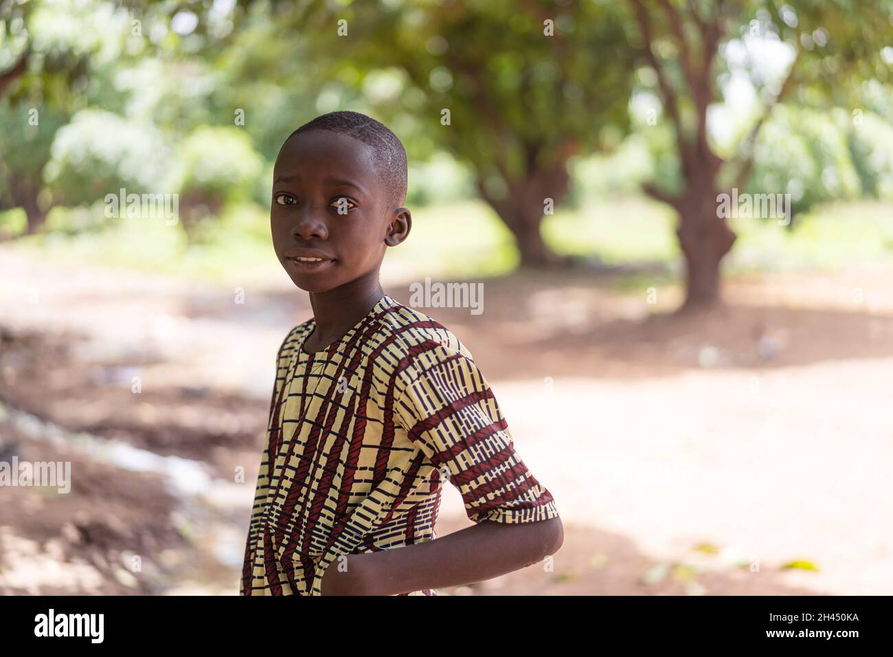 Lone black boy standing in a forest on the edge of an African village, looking thoughtfully into the camera Stock Photo