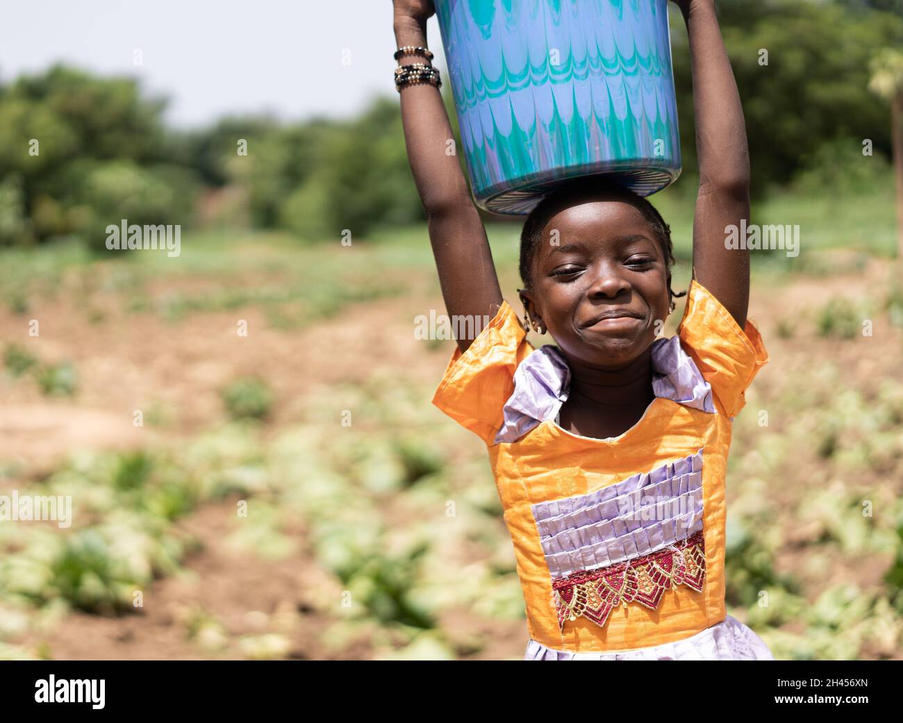 Smirky little black African village girl with a water canister on her head looking at the camera Stock Photo