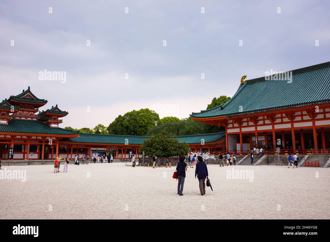 View of the inner courtyard of Heian Shrine with crowd of people walking. Main hall, Byakko-rou tower and cloudy sky background. Stock Photo