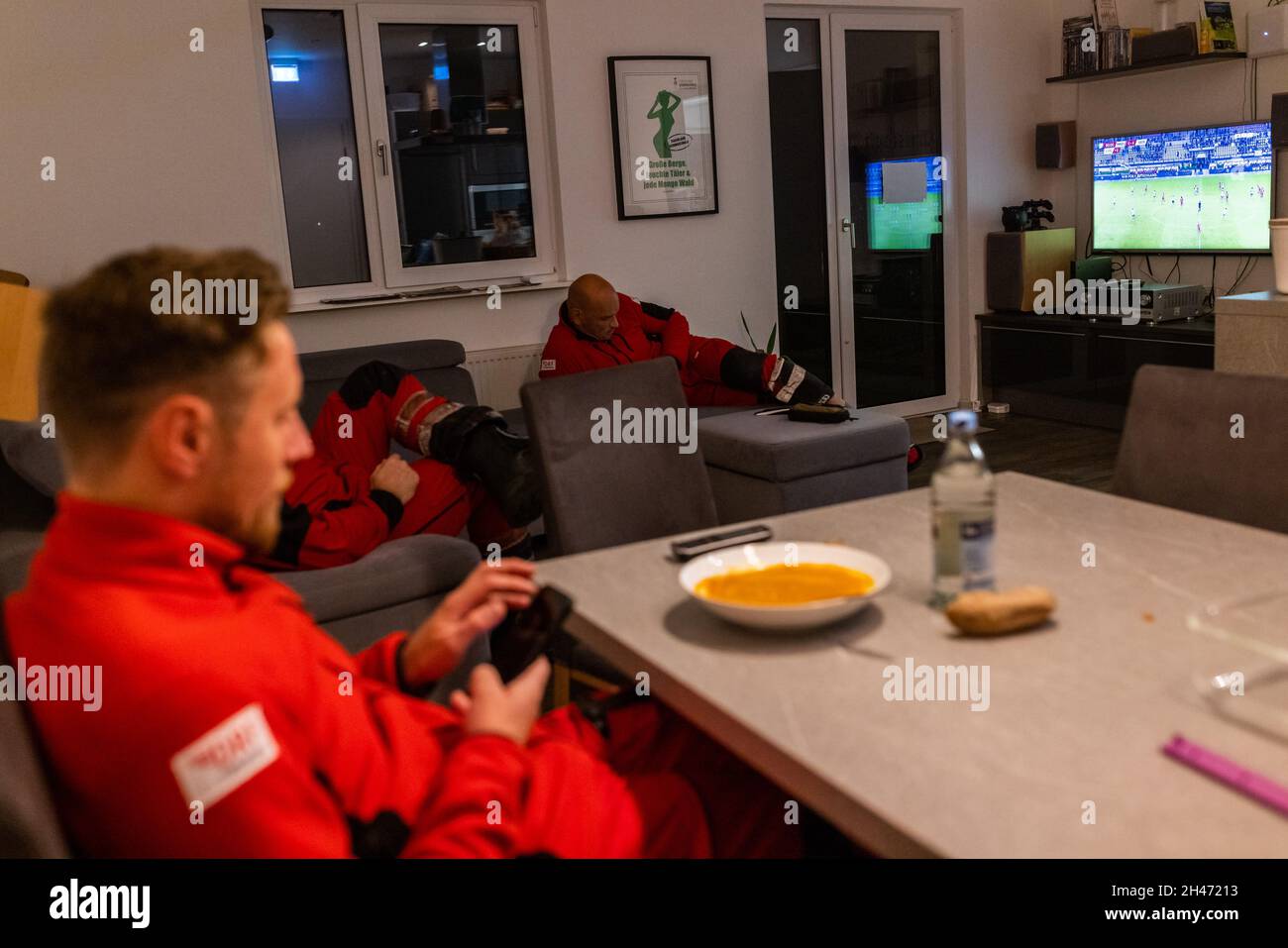 PRODUCTION - 11 October 2021, Baden-Wuerttemberg, Villingen-Schwenningen: The pilots of the rescue helicopter, Roy Fleischer (l-r) and Matthias Fleisch look at their smartphones while sitting in front of their dinner and lying on the sofa. The rescue helicopter Christoph 54 is the only one in Baden-Württemberg that also has night flight capacity. The night crew with the two pilots takes over the flying intensive care unit from 6.30pm in the evening until 7am the following morning. It is stationed at the Villingen-Schwenningen station of the German Air Rescue Service (DRF) and flies missions fr Stock Photo