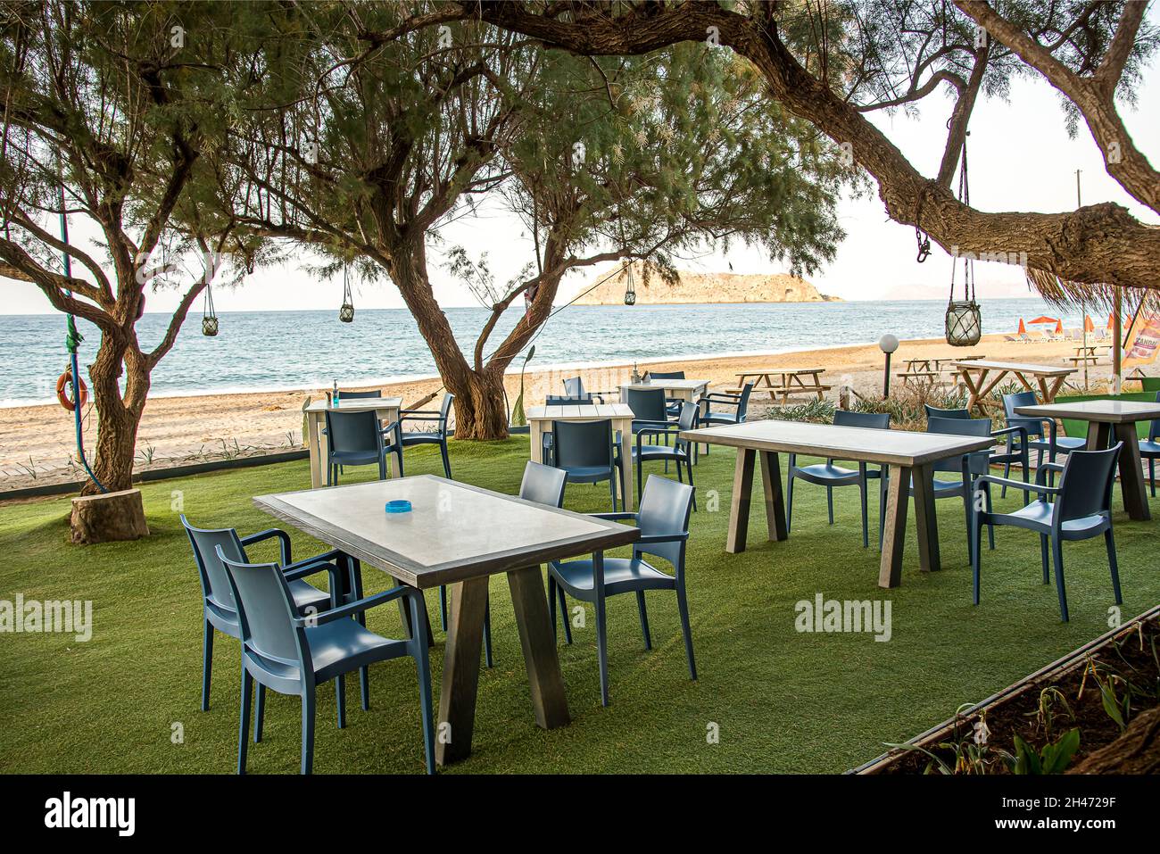traditional greek restaurant with blue tables and chairs under the trees at Platanias beach, Crete, October 7, 2021 Stock Photo
