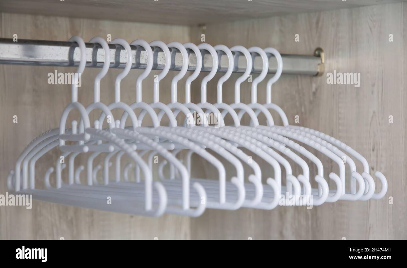 Silver horizontal metal rail with group of white empty plastic clothe hangers in row in wooden closet. Organize storage boutique store accessory, disc Stock Photo