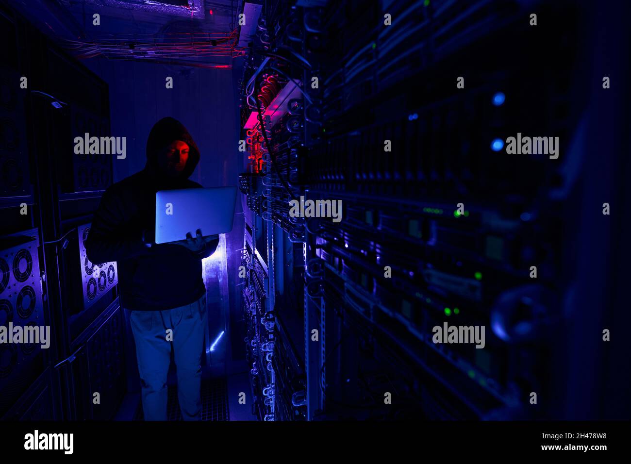 Cybercrook typing on notebook in server room Stock Photo