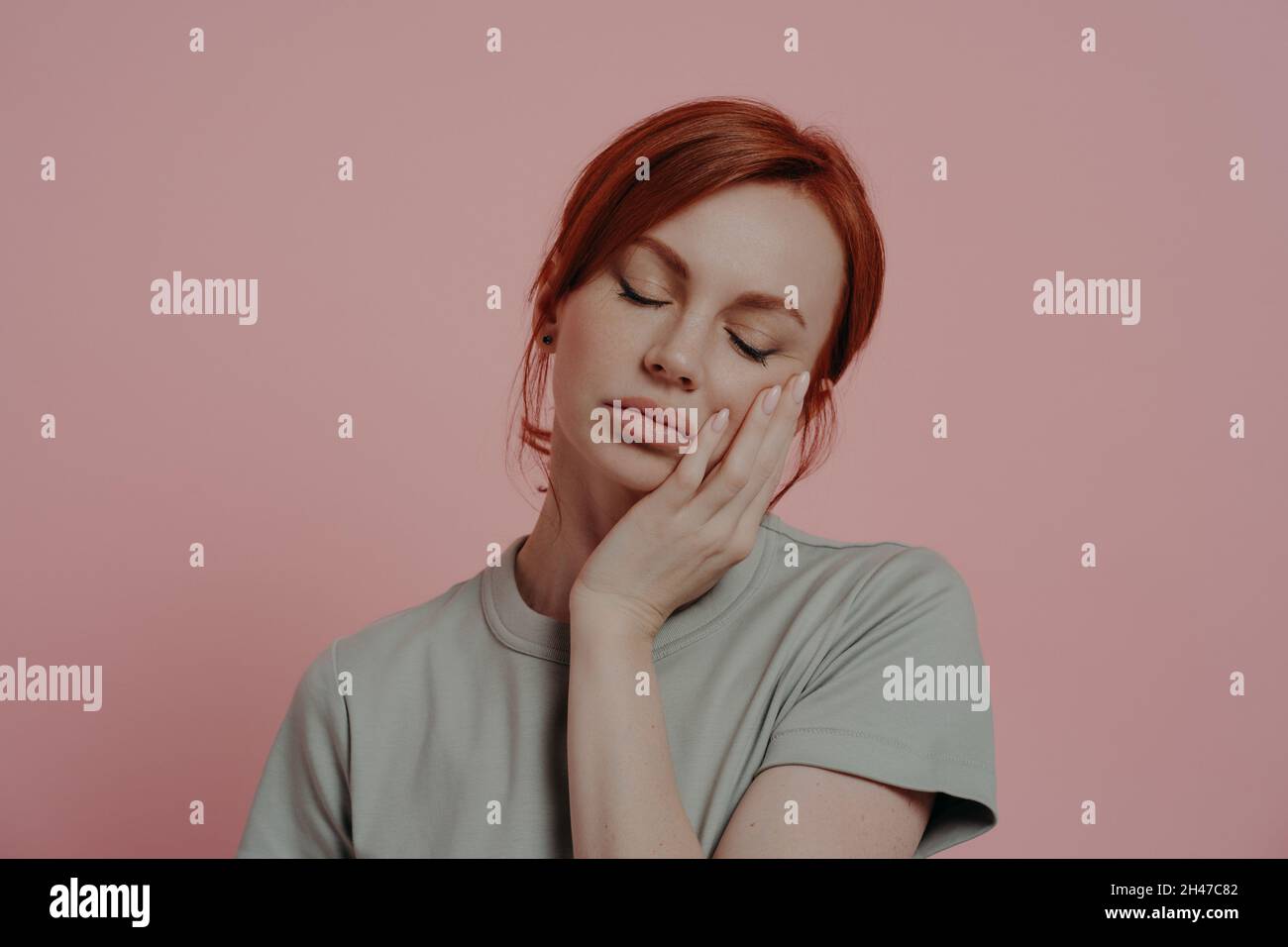 Sleepy tired red-haired woman dozing on hand, falling asleep, isolated over pink background Stock Photo